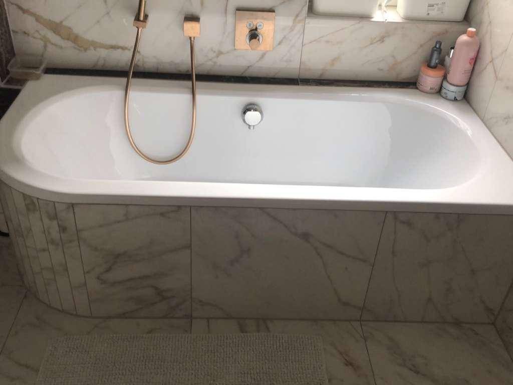 Elegante Badewanne mit Marmorverkleidung und modernen Armaturen in Goldoptik im Badezimmer.