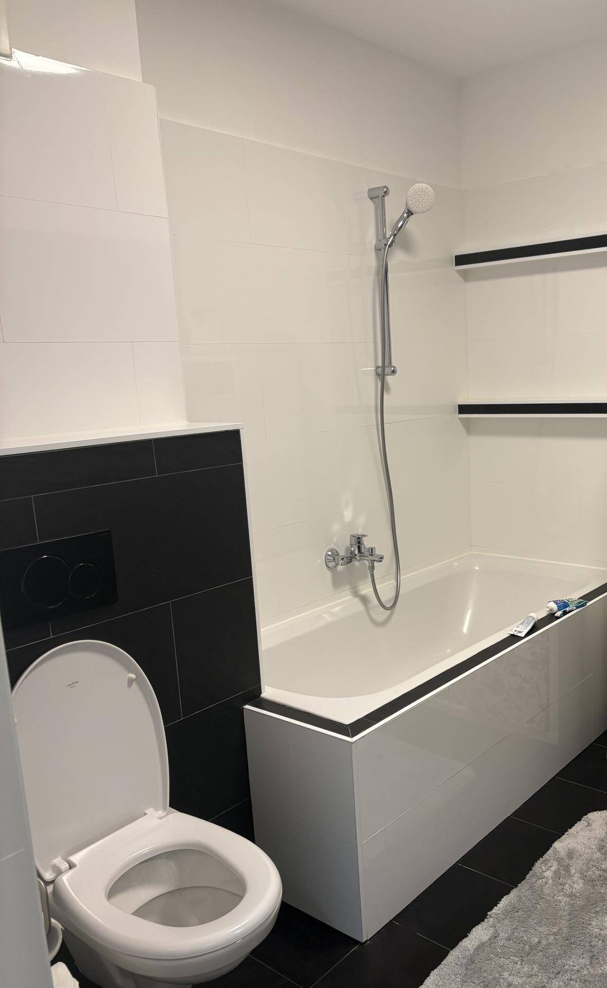 Modernes Badezimmer mit Badewanne, Wand-WC und schwarz-weißen Fliesen.