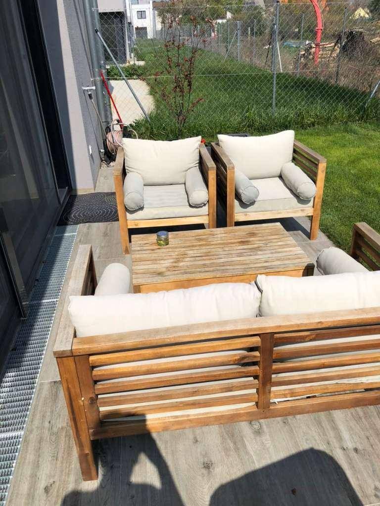 Sonnige Terrasse mit bequemen Holzmöbeln und angrenzendem gepflegten Rasenbereich.