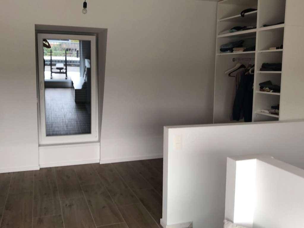 Heller Raum mit Holzoptik-Fliesenboden und integriertem Kleiderschrank, mit Zugang zur Terrasse.