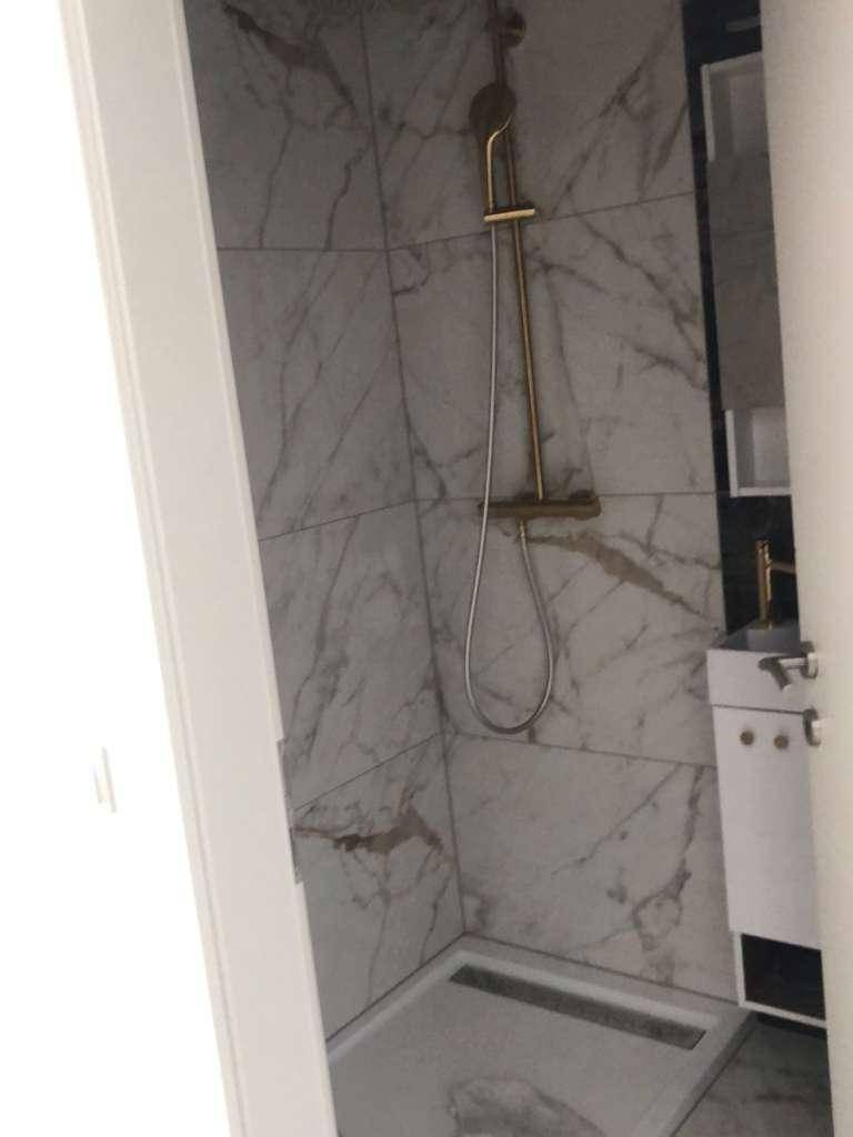 Modernes Badezimmer mit eleganten Marmorfliesen und goldfarbener Duscharmatur in der Duschkabine.