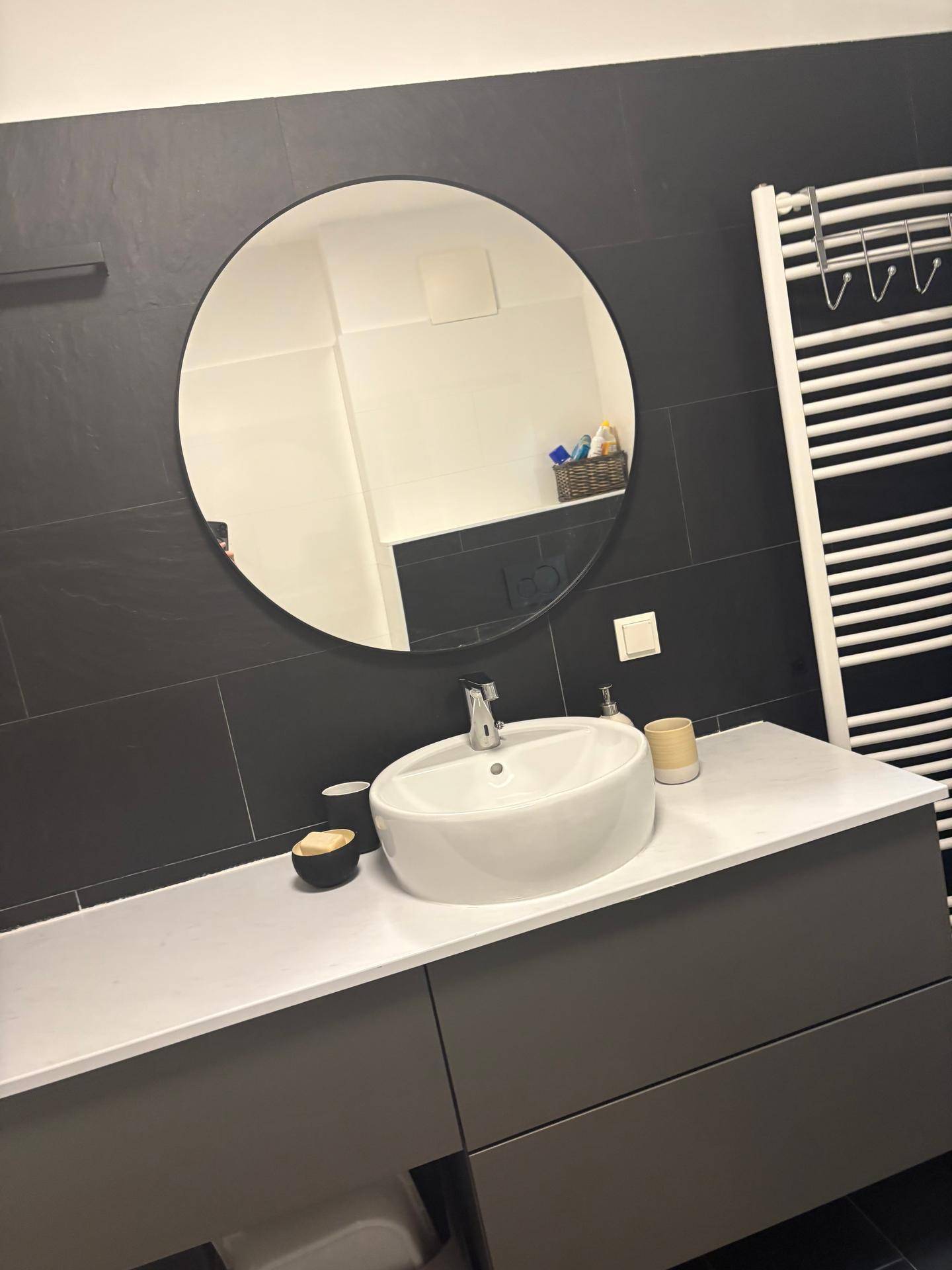 Modernes Badezimmer mit Waschtisch, rundem Spiegel und beheiztem Handtuchhalter.