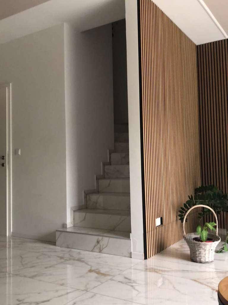 Heller Eingangsbereich mit Marmorfliesen, Treppe und dekorativer Holzlamellenwand als Akzent.