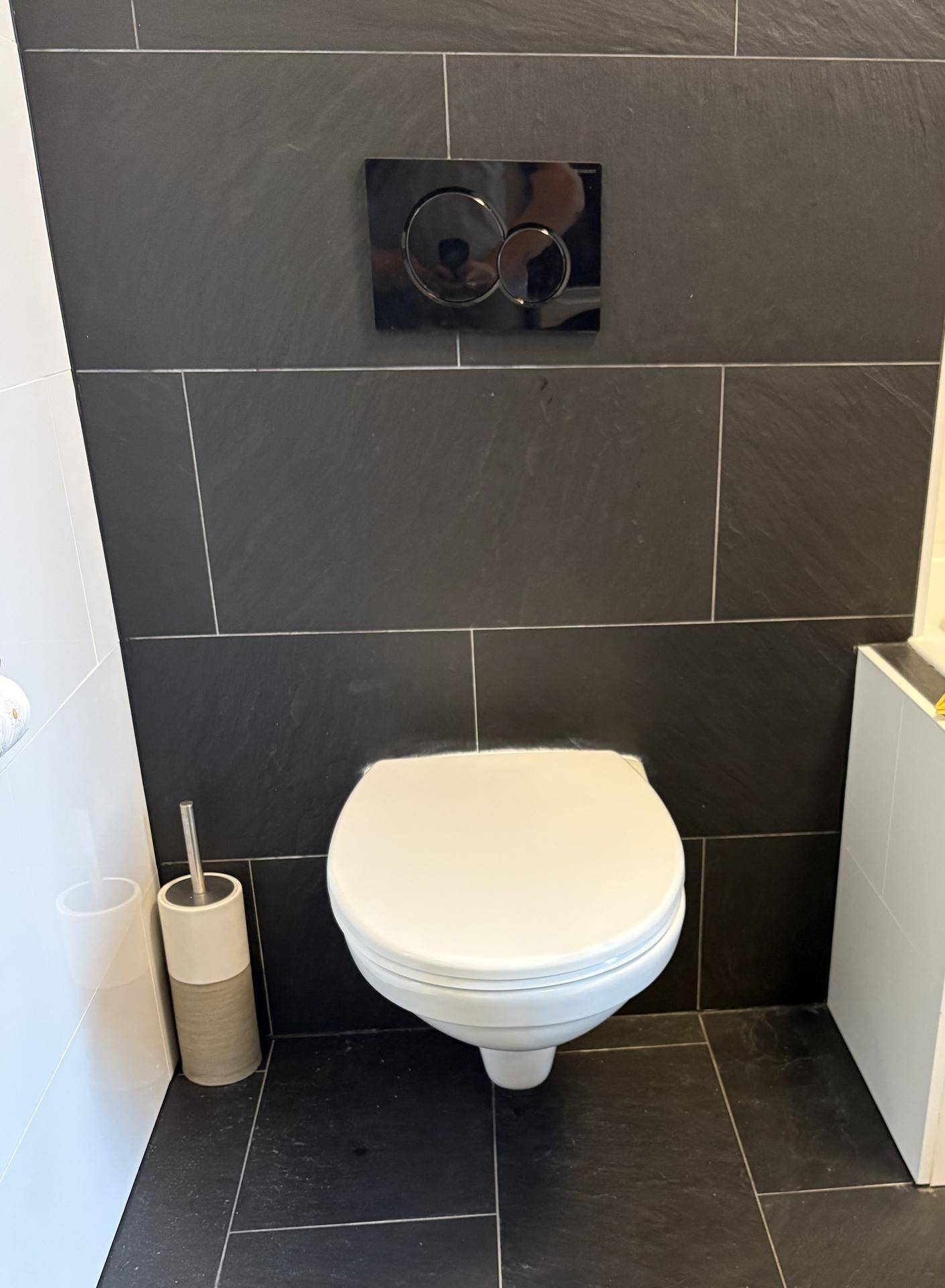 Modernes Gäste-WC mit Wand-WC und dunklen Fliesen an der Wand.