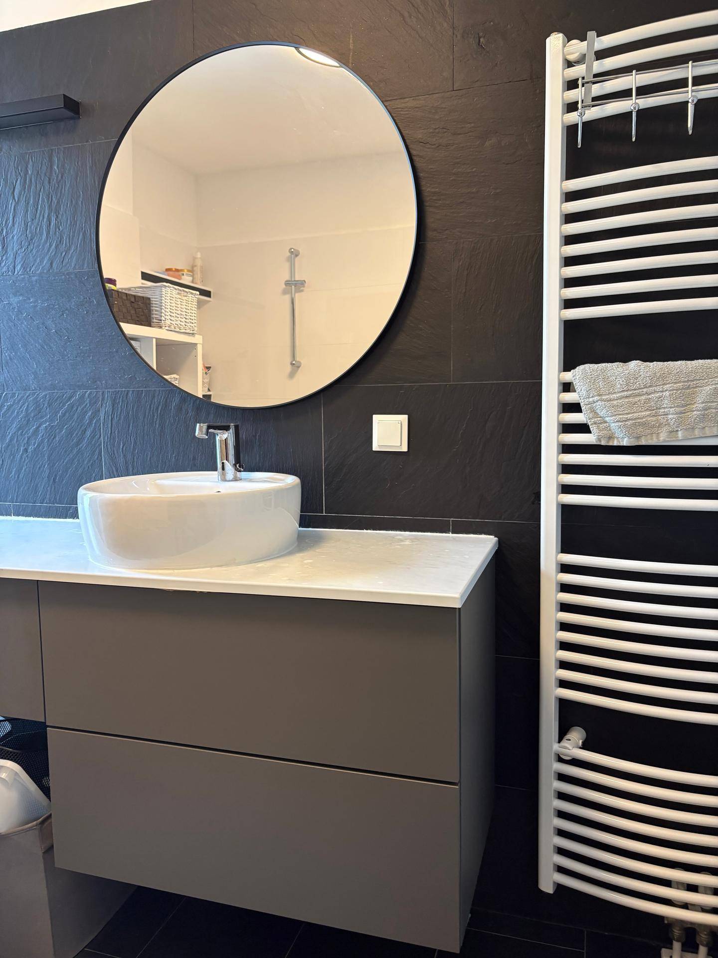Modernes Badezimmer mit rundem Spiegel, Waschtisch und beheiztem Handtuchhalter.