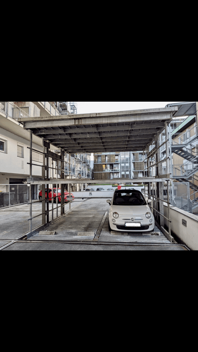 Frontansicht des mechanischen Parksystems mit einem weißen Fiat 500 und umliegenden Gebäuden.