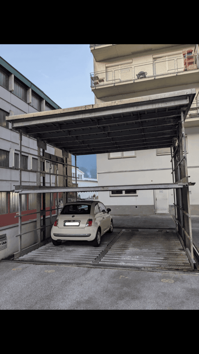 Rückansicht des mechanischen Parksystems mit einem weißen Auto und angrenzendem Wohngebäude.