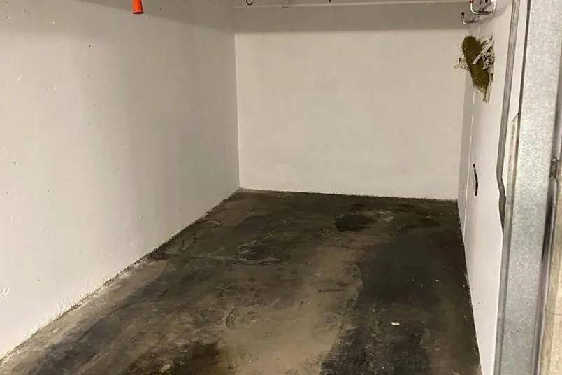 Innenansicht einer Garage mit schmutzigem Betonboden und einfachen weißen Wänden.