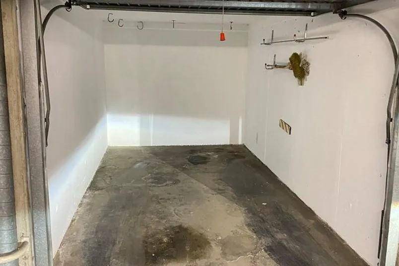 Leere Garage mit weißen Wänden, Betonboden und praktischen Haken zur Aufbewahrung von Gegenständen.