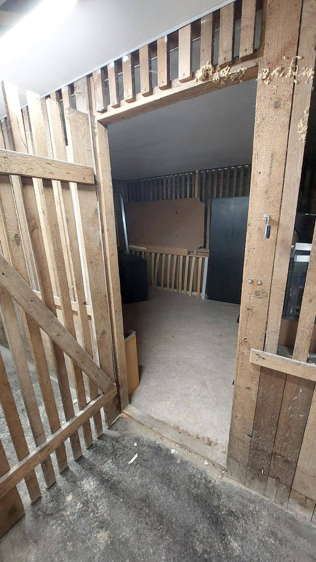 Blick durch eine Holztür in einen Raum im Rohbau mit sichtbaren Holzstrukturen und Betonboden.