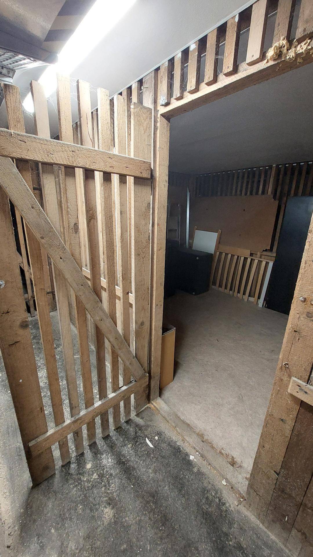 Innenraum im Rohbau mit Holztür und freiliegenden Holzlattenwänden, Blick in einen weiteren Bereich.