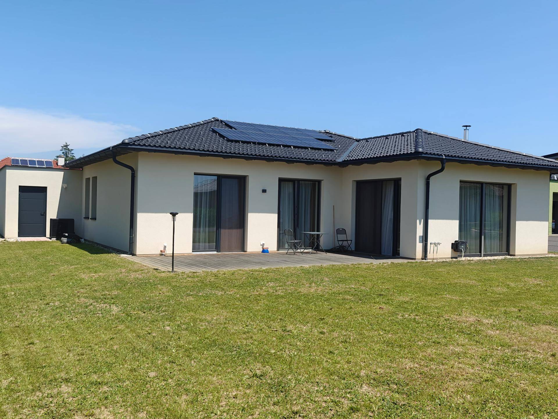 Neubau mit weitläufigem Garten, Holzterrasse und Photovoltaikanlage auf dem Dach.
