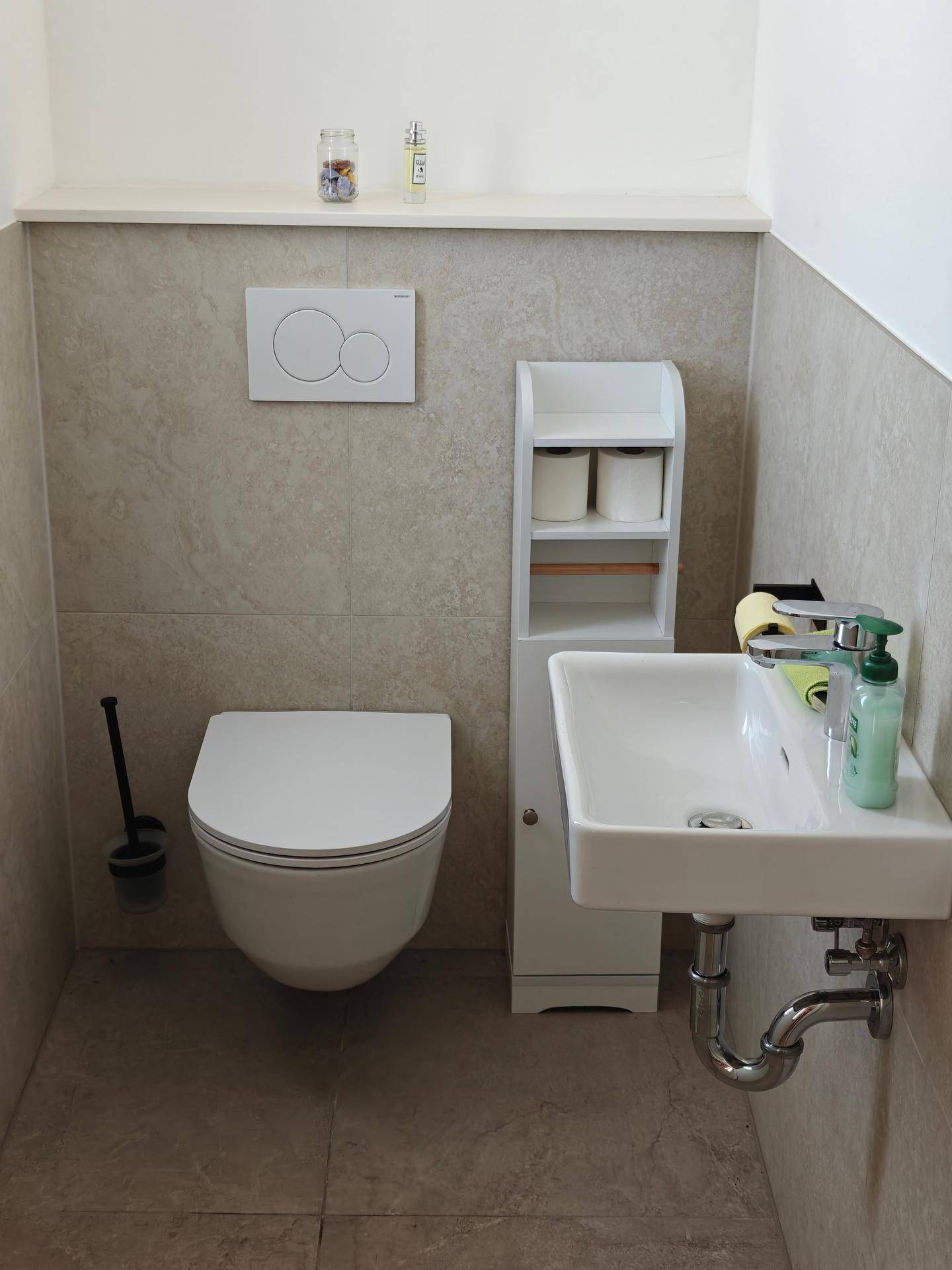 Modernes Gäste-WC mit wandhängendem WC, kleinem Waschbecken und hellen Fliesen.