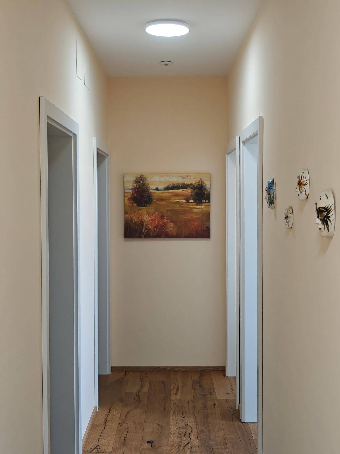 Langer Flur mit hellem Holzboden und einem Landschaftsbild an der beigefarbenen Wand.