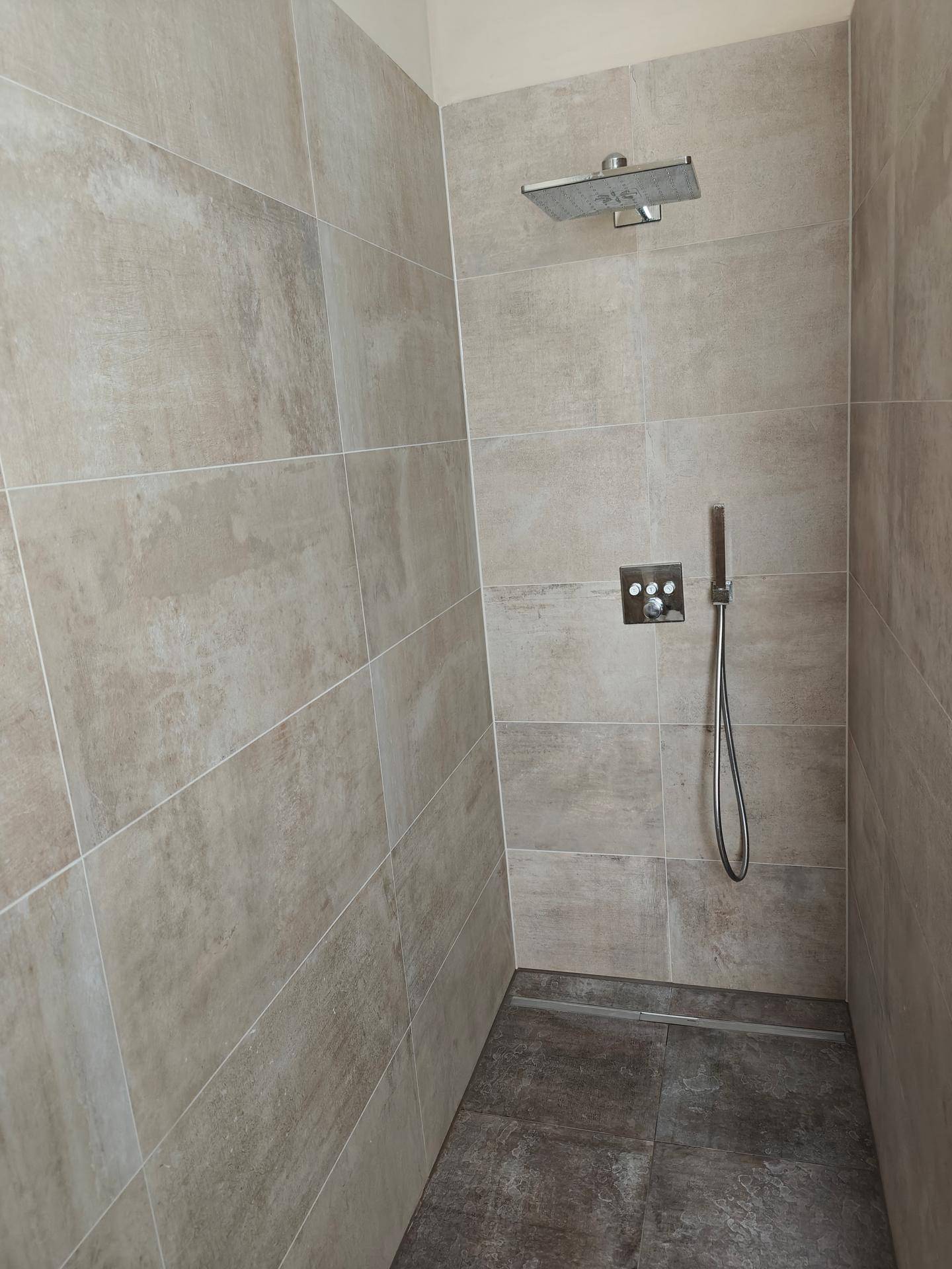 Geräumige begehbare Dusche mit großformatigen Fliesen und einer modernen Regendusche.