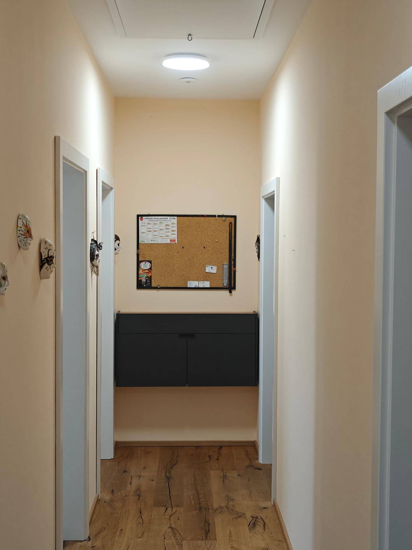 Flur mit Holzboden, einer Pinnwand und einem dunklen Hängeschrank an der Wand.