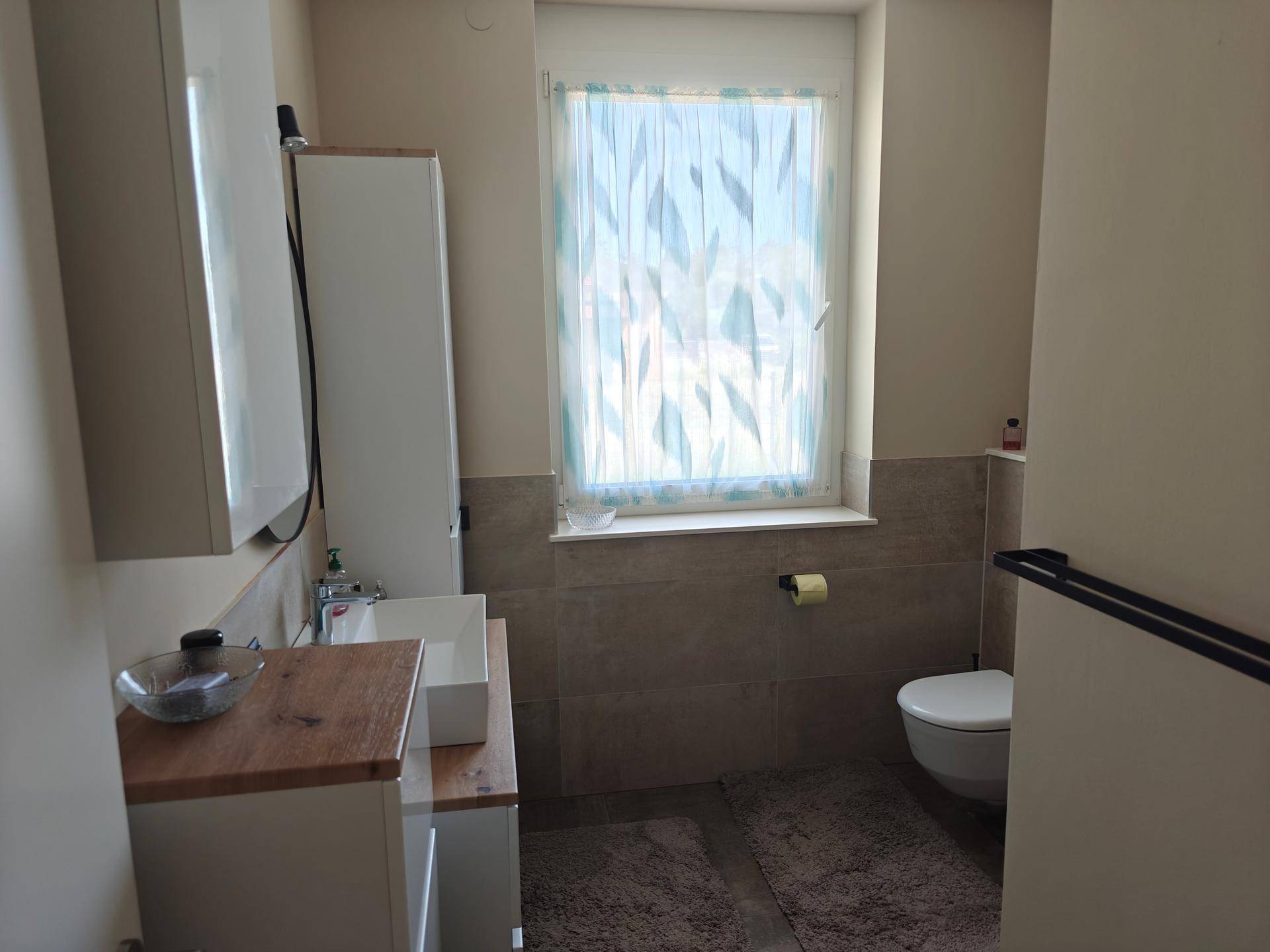 Helles Badezimmer mit WC, modernem Waschtisch und einem Fenster für Tageslicht.