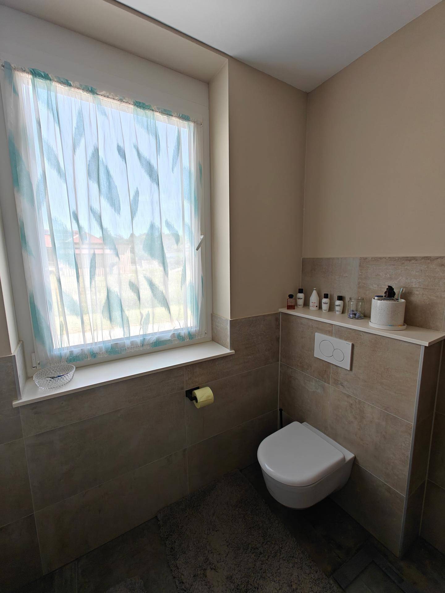 Badezimmer mit wandhängendem WC und einem Fenster, das für natürliche Belüftung sorgt.