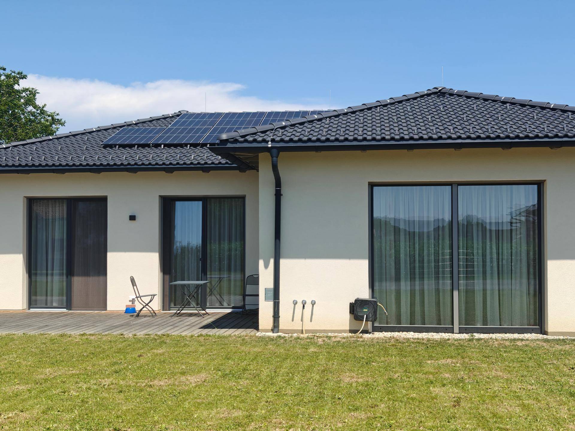 Rückseite des Hauses mit Holzterrasse, Garten und Photovoltaikanlage auf dem Dach.