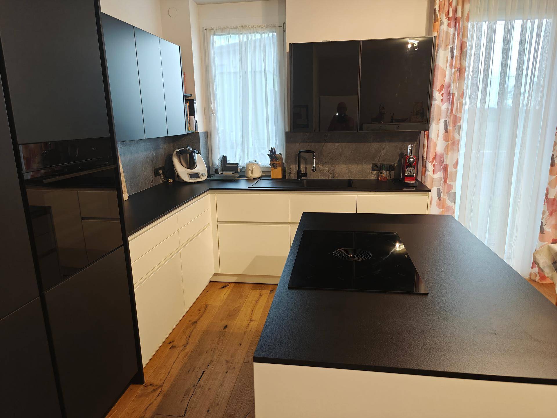 Helle moderne Küche mit Kochinsel, schwarzen und weißen Elementen und einem Fenster mit Vorhängen.
