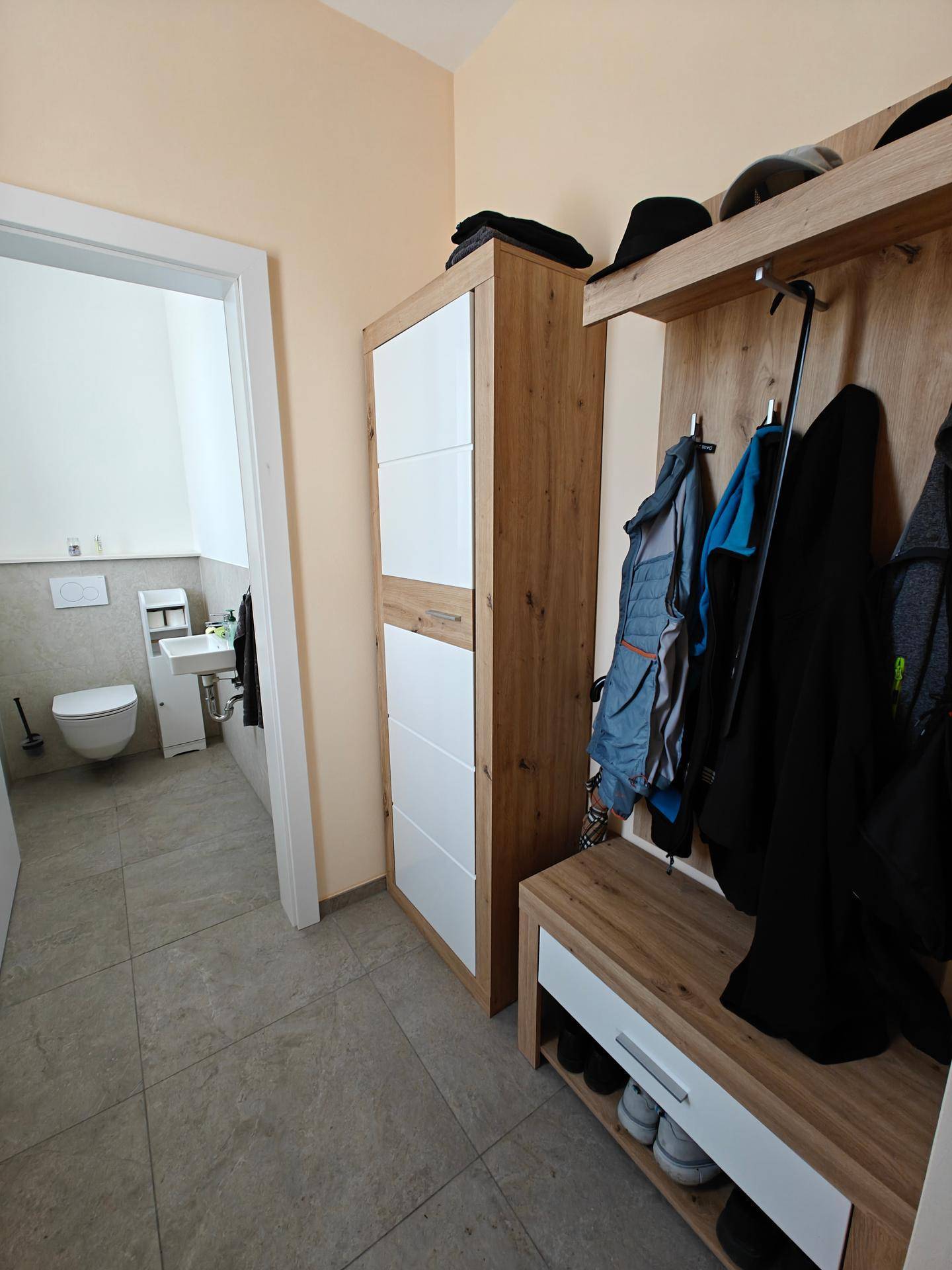 Flur mit Garderobe und Schuhbank, der einen Blick in das angrenzende Gäste-WC ermöglicht.