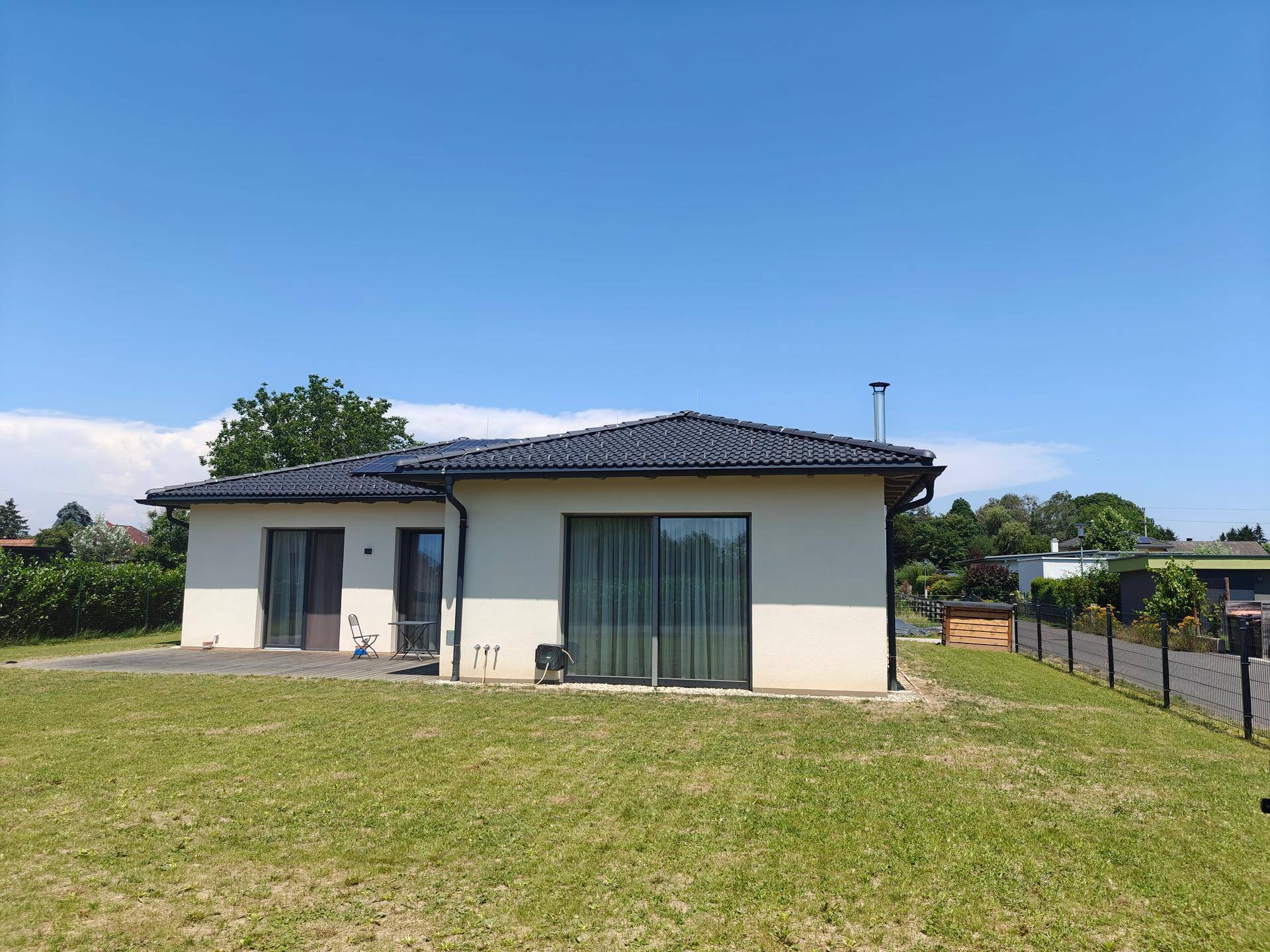 Modernes Einfamilienhaus mit großem Garten und Schiebetüren zur Terrasse unter blauem Himmel.