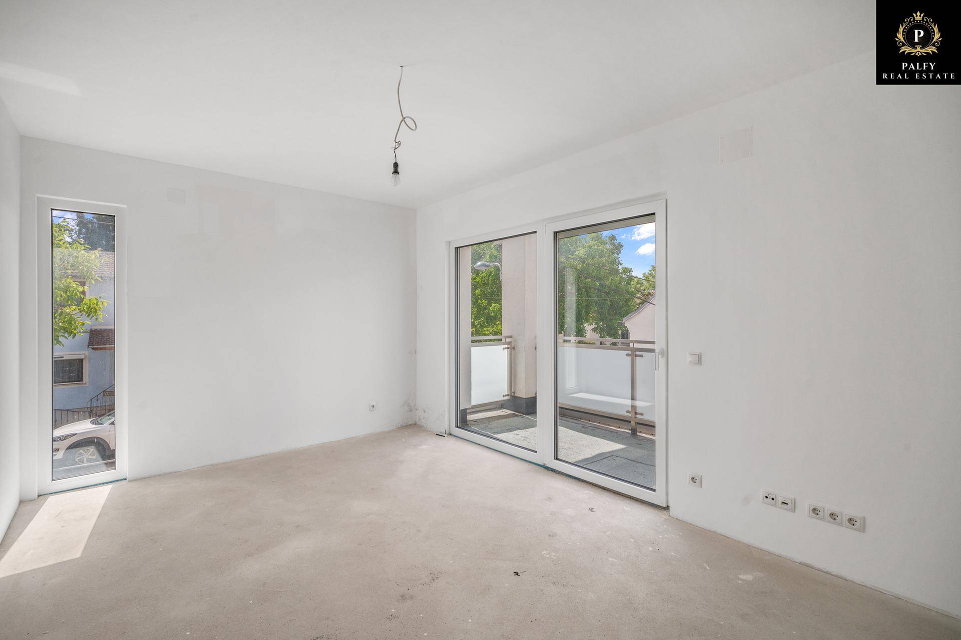 Heller, unmöblierter Raum im Rohbau mit großen Fenstern und Zugang zu einem Balkon.