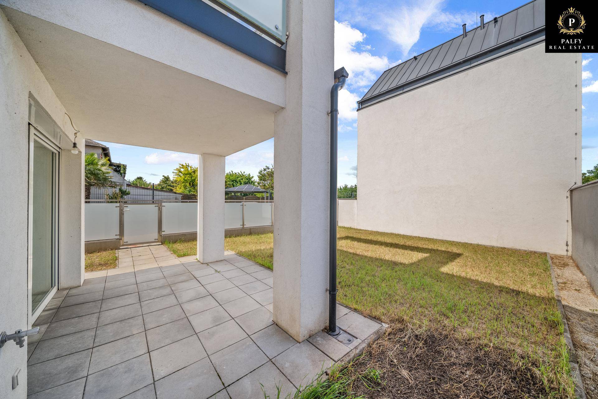 Überdachte Terrasse mit Fliesenboden und Zugang zum kleinen privaten Gartenbereich des Neubaus.