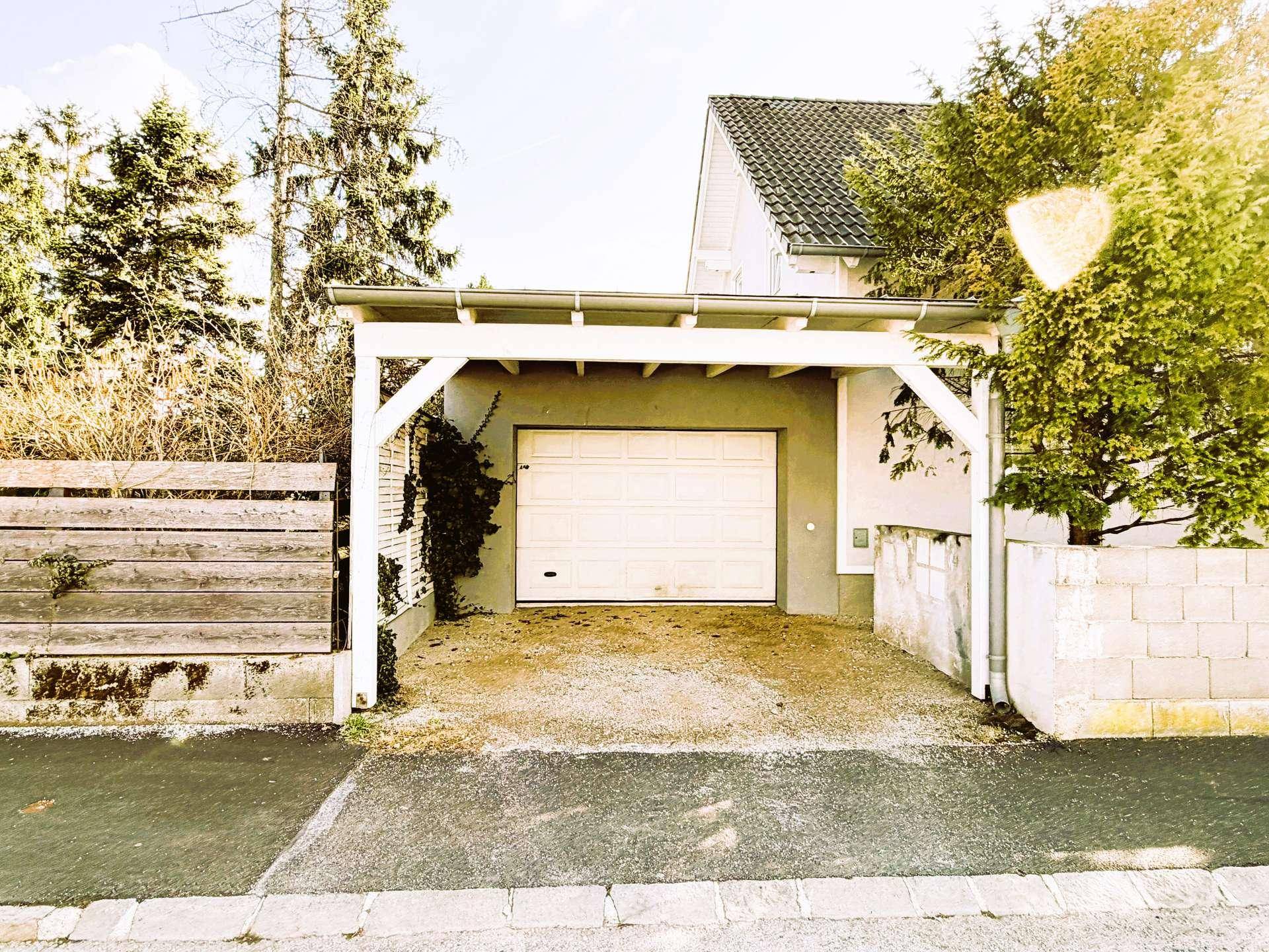 Überdachter Carport und eine Garage mit weißem Rolltor, direkt an der Straße gelegen.