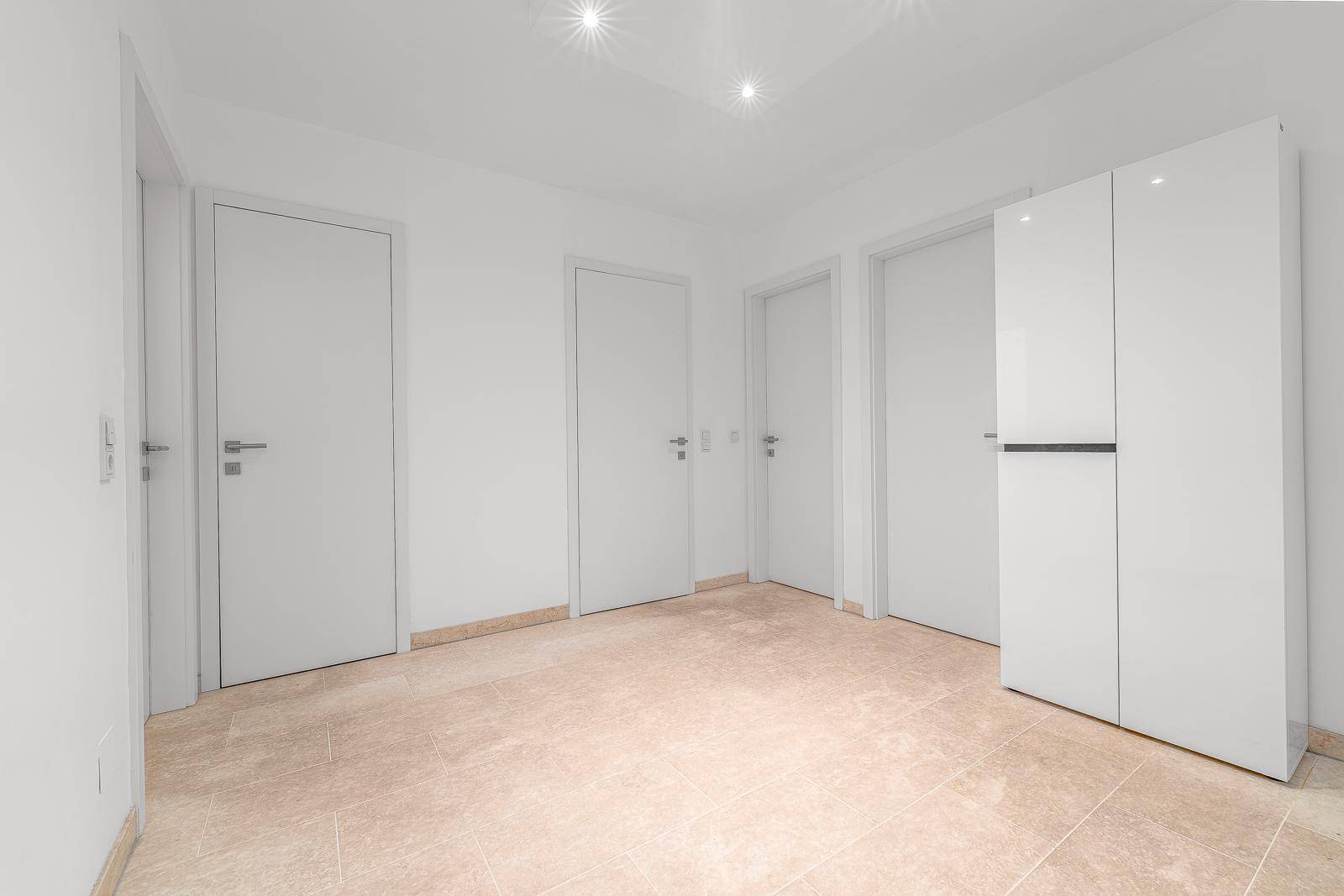 Geräumiger Flur mit hellen Fliesen, weißen Türen und einem modernen Schrank.