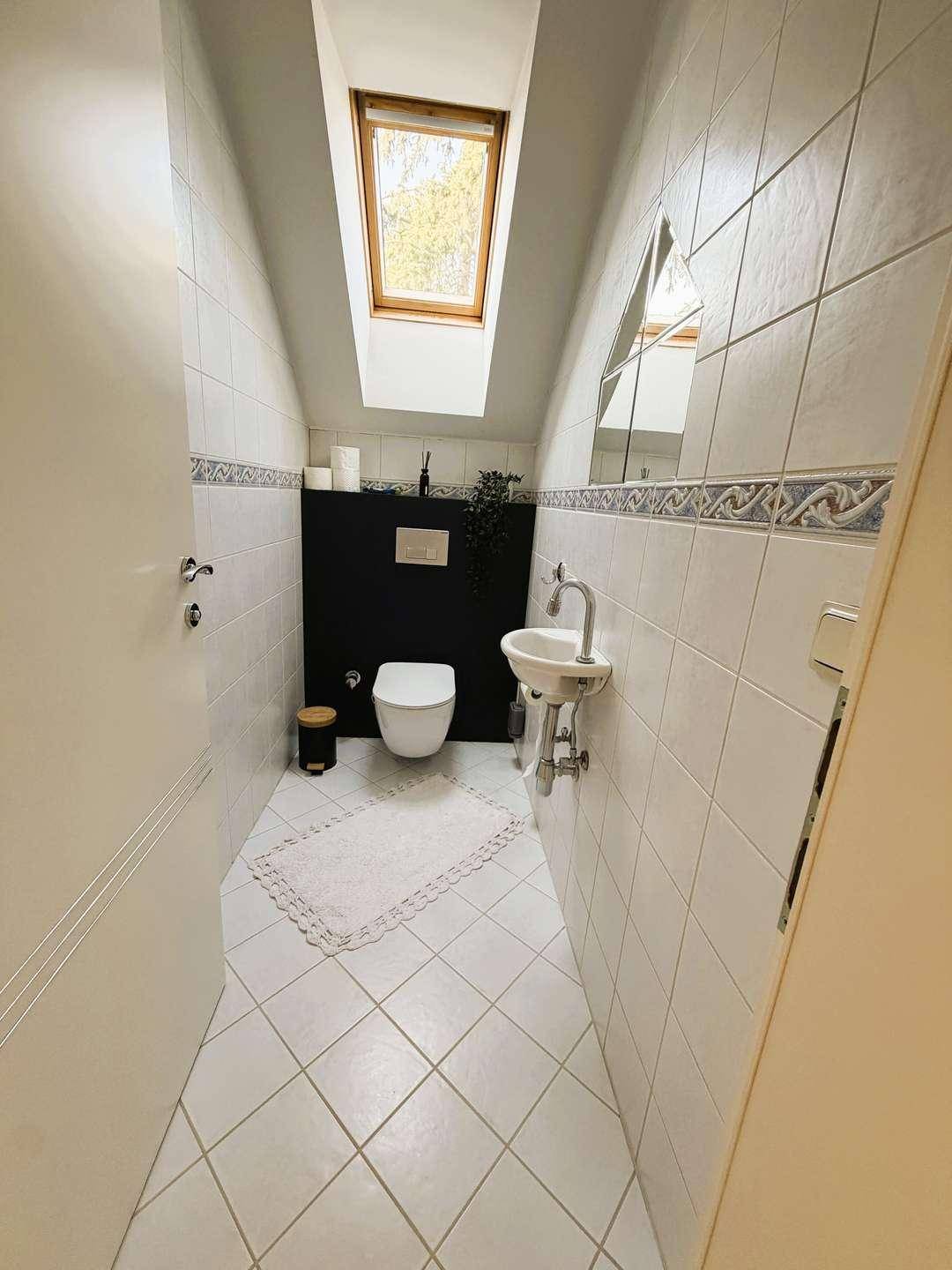 Kleines Gäste-WC im Dachgeschoss mit Hänge-WC, Handwaschbecken und einem praktischen Dachfenster.