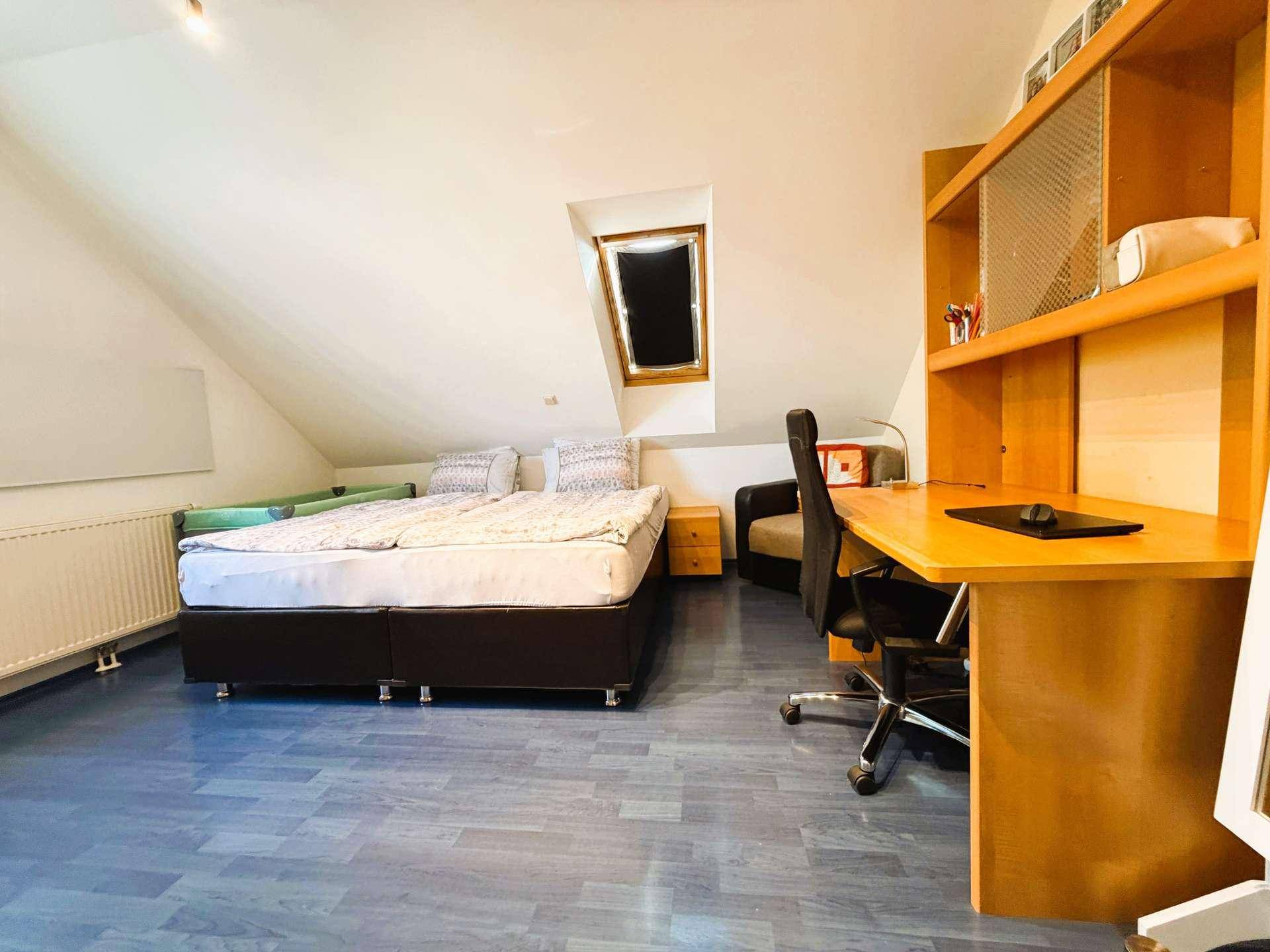 Helles Schlafzimmer im Dachgeschoss mit Doppelbett, Schreibtisch und einem Dachfenster für zusätzliches Licht.