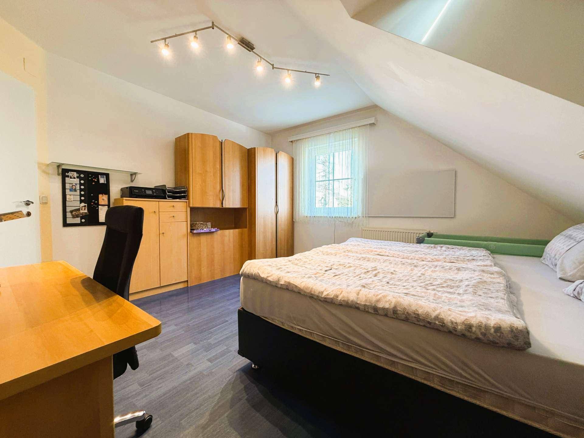 Geräumiges Schlafzimmer im Dachgeschoss mit Doppelbett, Kleiderschrank und einem Fenster für natürliche Belichtung.