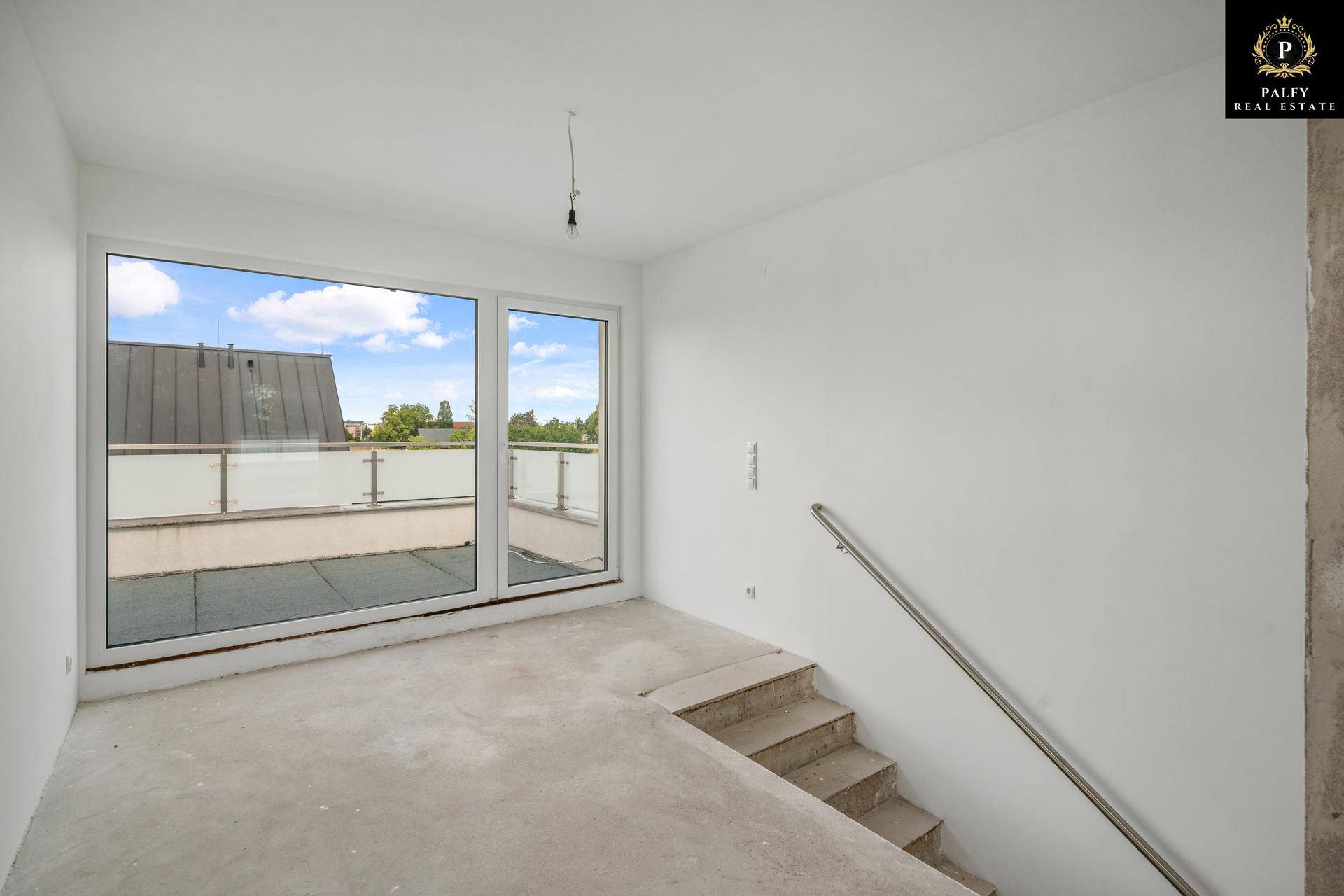Unmöblierter Raum im Rohbau mit Treppe und großen Fenstern zur Dachterrasse.
