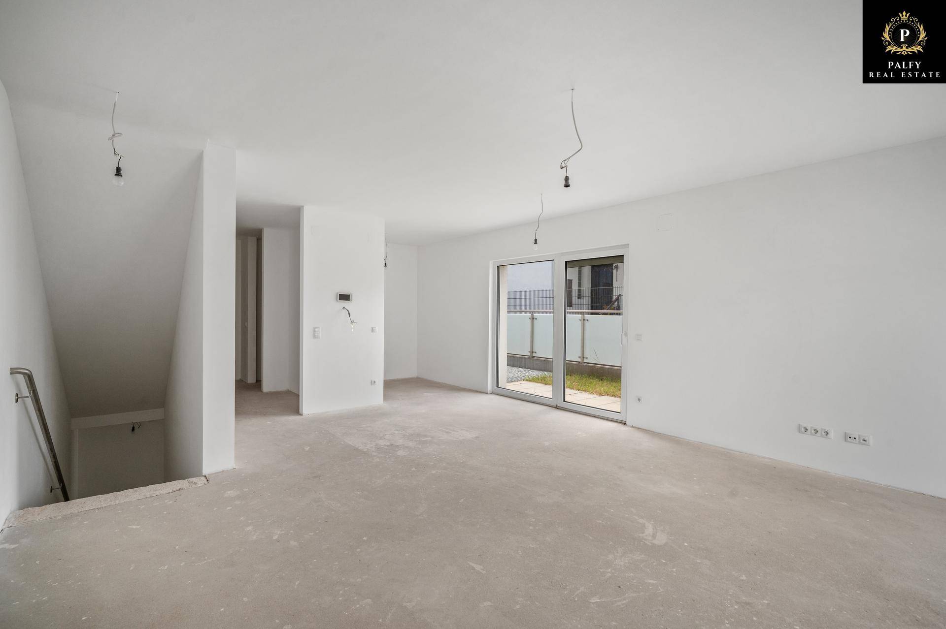 Heller, unmöblierter Raum im Rohbau mit Treppenaufgang und Zugang zu einem Balkon.