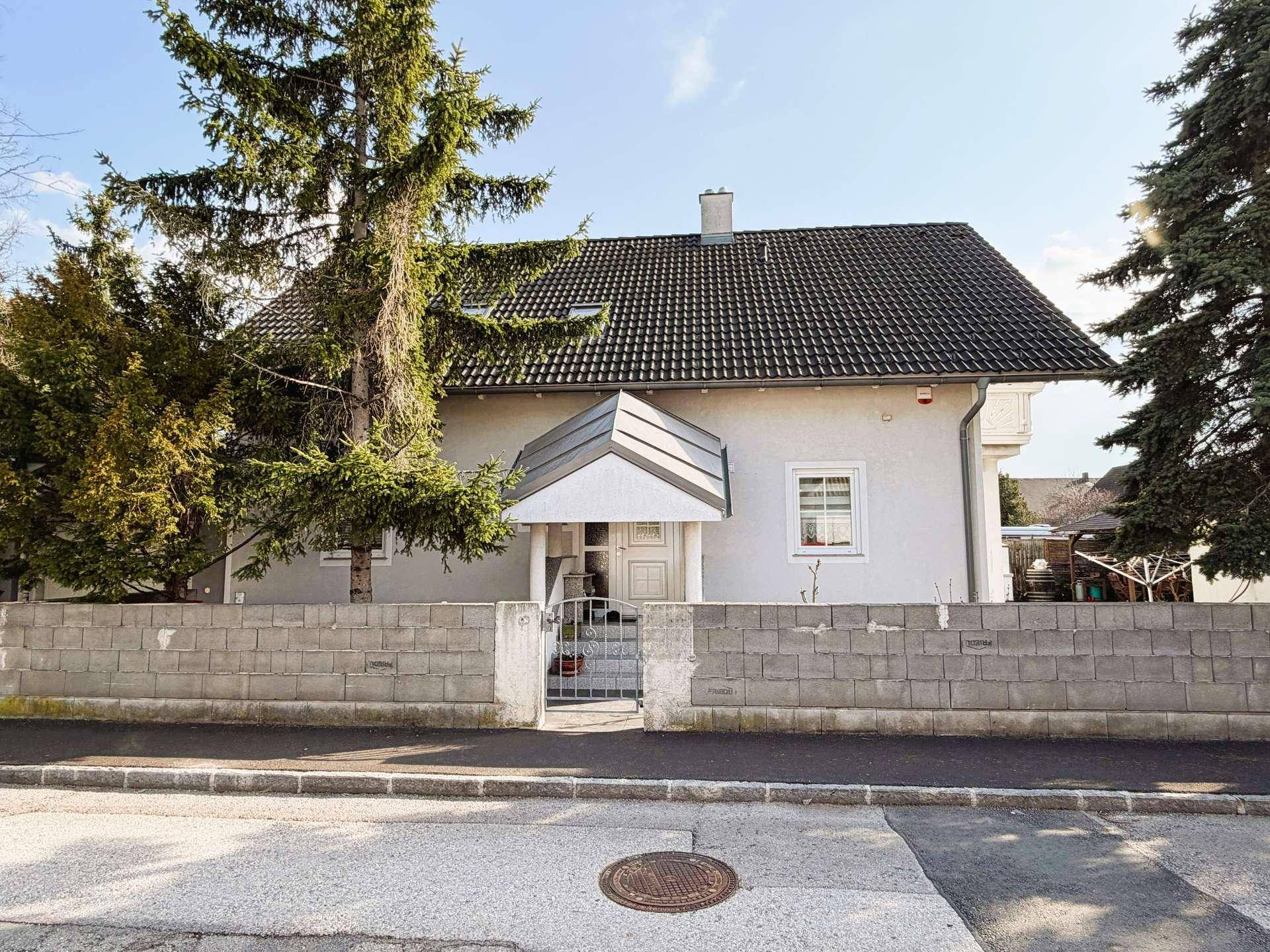 Vorderansicht des Einfamilienhauses mit grauer Fassade, umzäuntem Vorgarten und Satteldach.