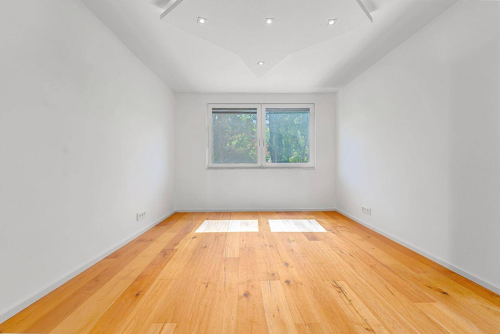 Helles, leeres Zimmer mit Holzboden und Einbaustrahlern in der Decke.