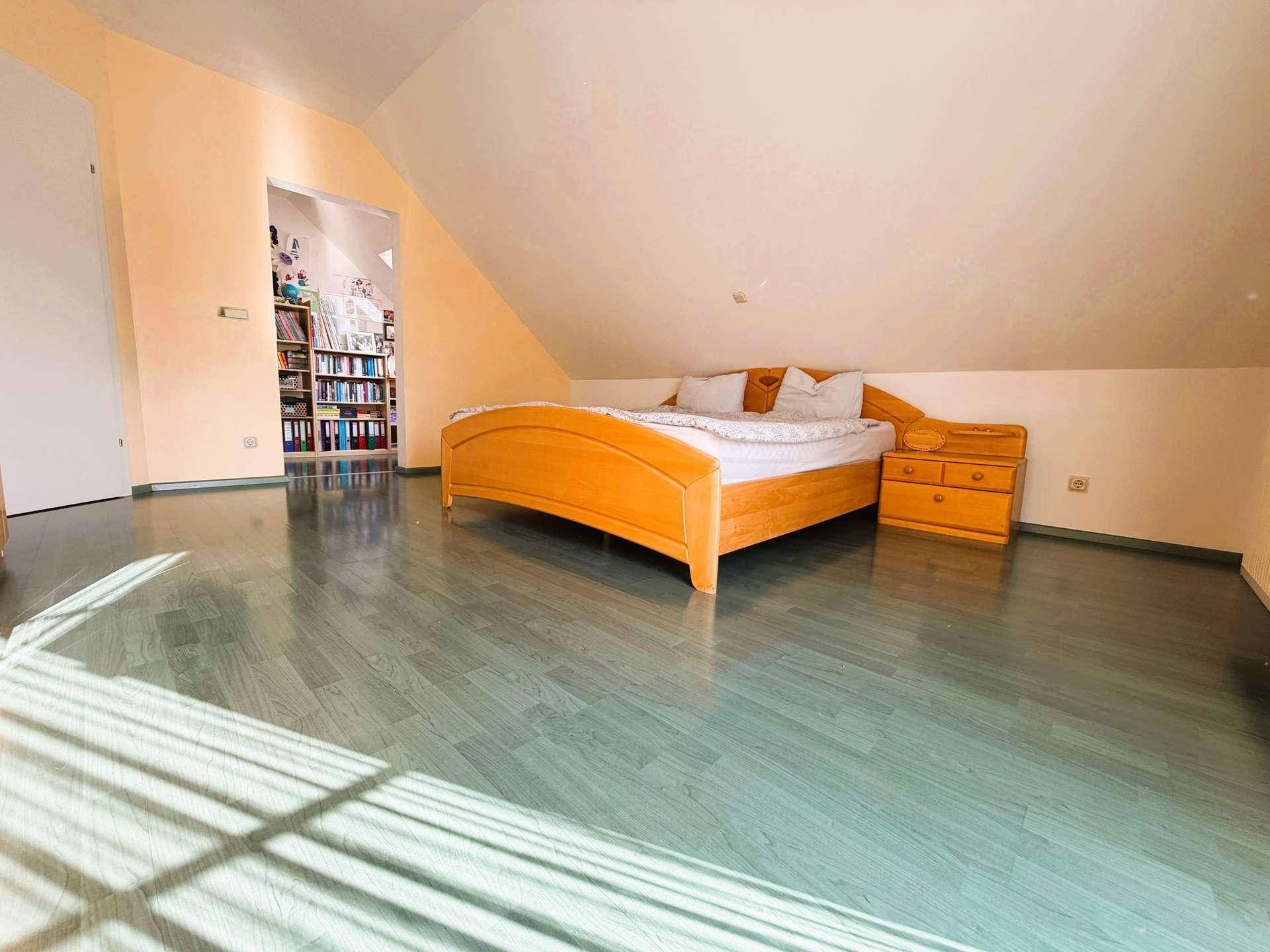 Gemütliches Schlafzimmer im Dachgeschoss mit schrägen Wänden, Holzbett und einem auffälligen grün-blauen Laminatboden.