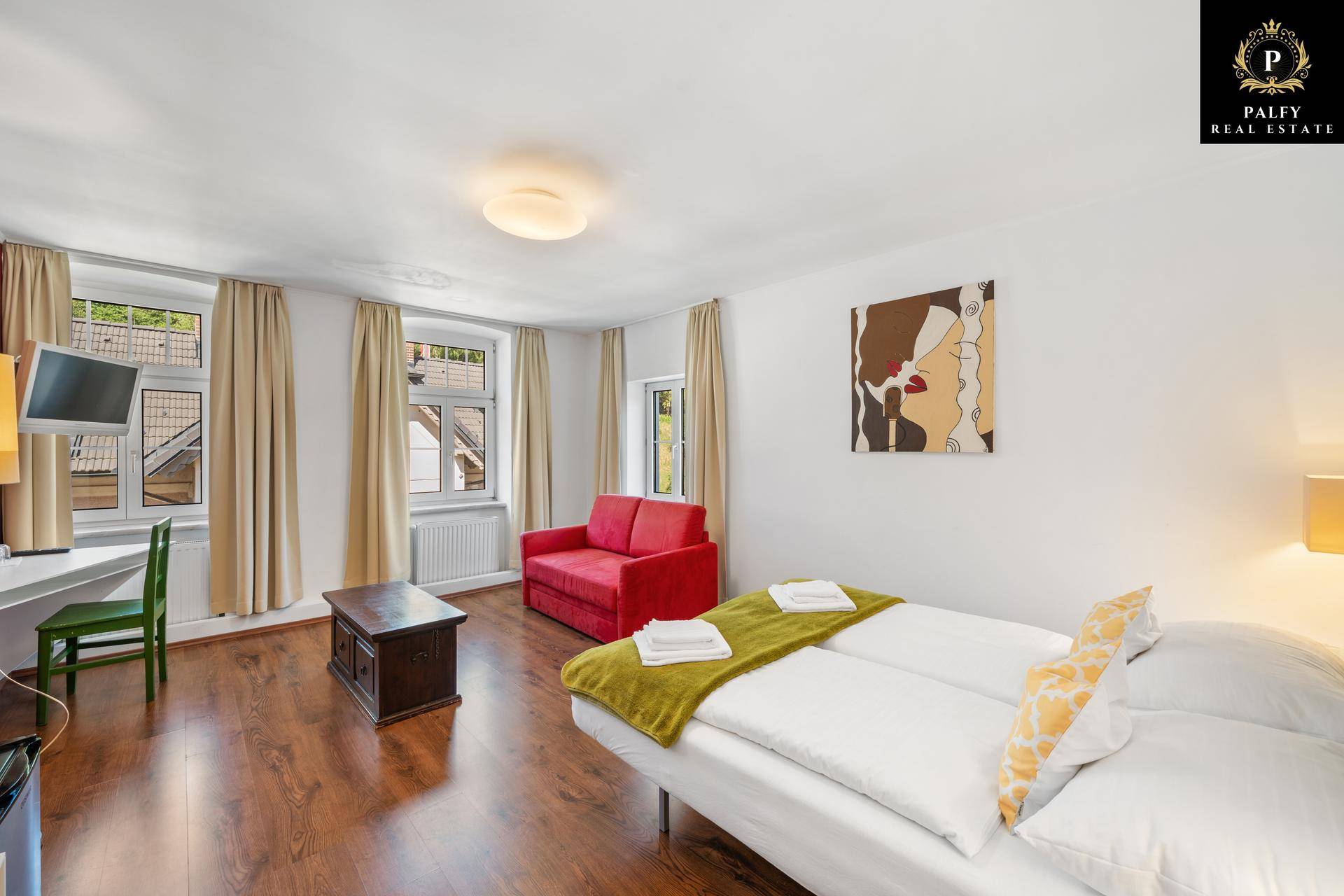 Gemütliches Schlafzimmer mit zwei Einzelbetten, rotem Sofa und Holzboden, hell und freundlich.