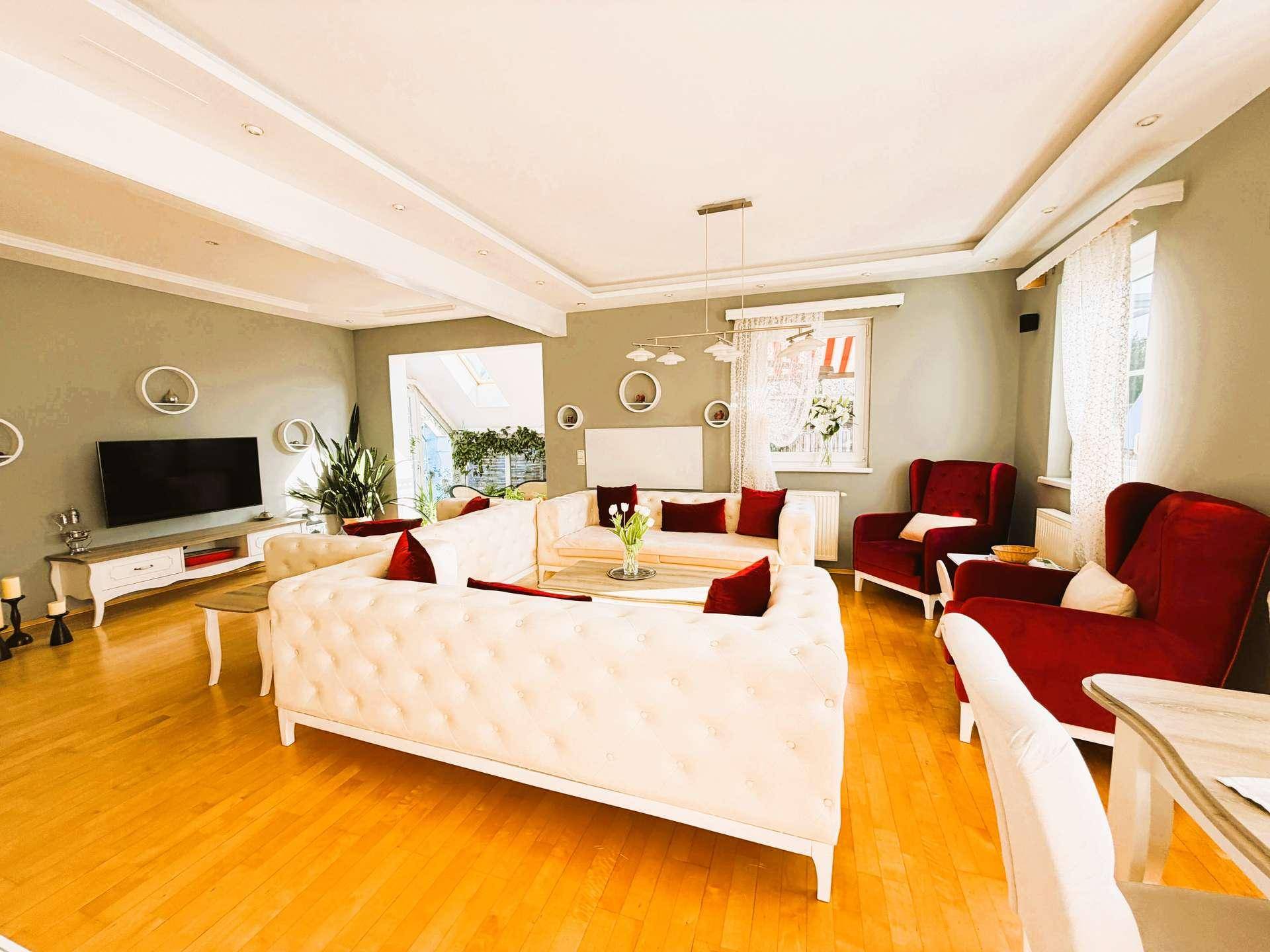 Geräumiger Wohnbereich mit Parkettboden, stilvollen Sofas und roten Akzenten, gut beleuchtet.