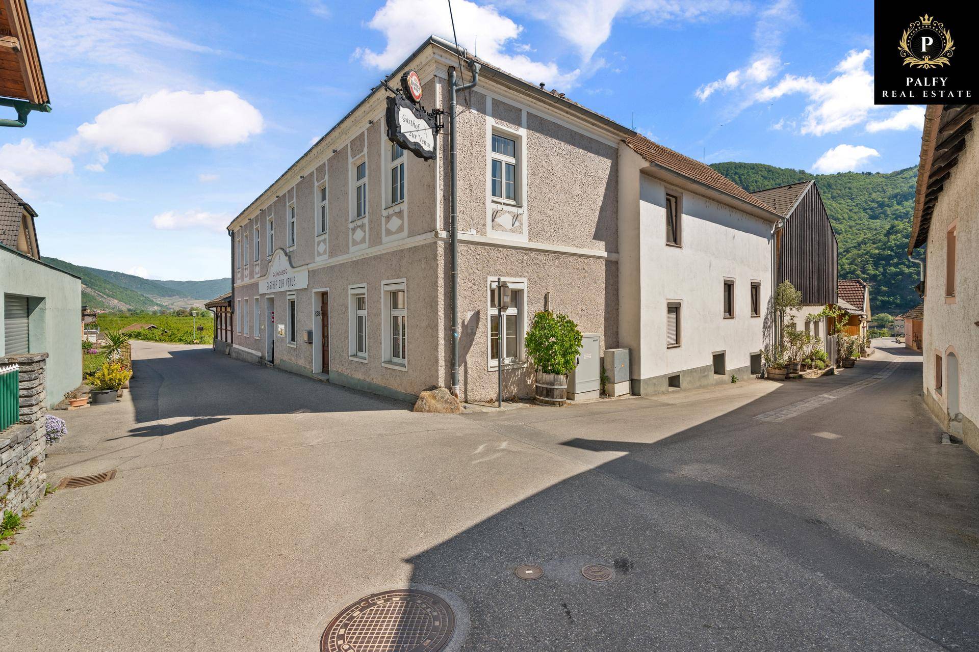 Ansicht eines traditionellen Gasthofs mit beiger Fassade und grünen Bergen im Hintergrund.