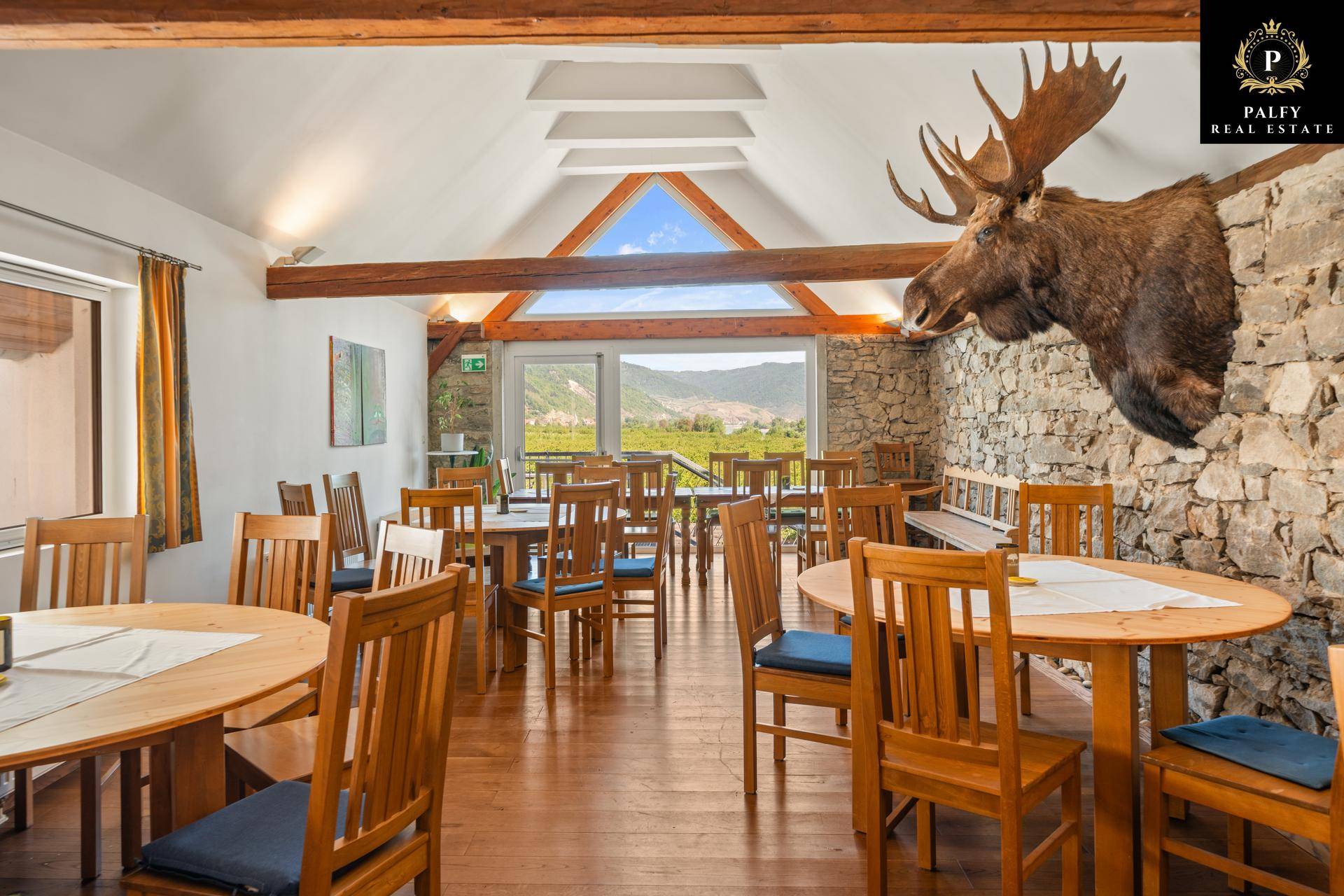 Rustikaler Speisesaal mit Holztischen, Steinwand und Blick auf die umliegende Natur.