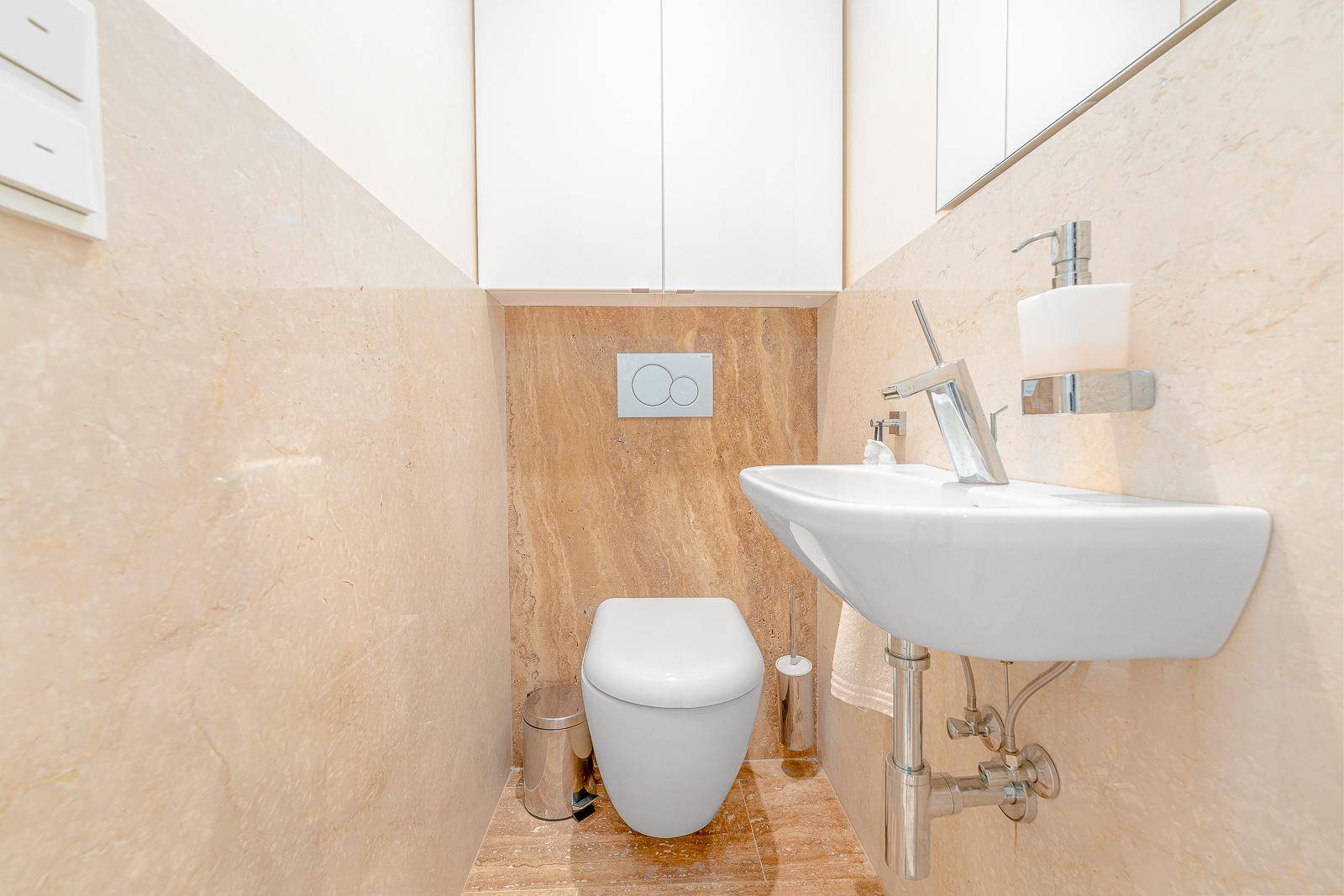 Kleines Gäste-WC mit Wand-WC, Waschbecken und beigefarbenen Fliesen.