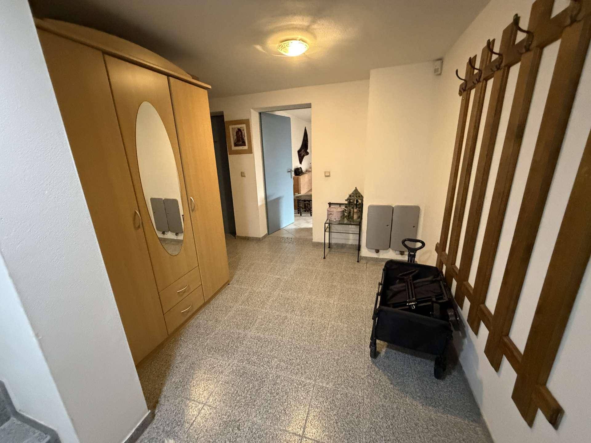 Geräumiger Flur im Kellergeschoss mit großem Kleiderschrank und Garderobe auf grauem Fliesenboden.