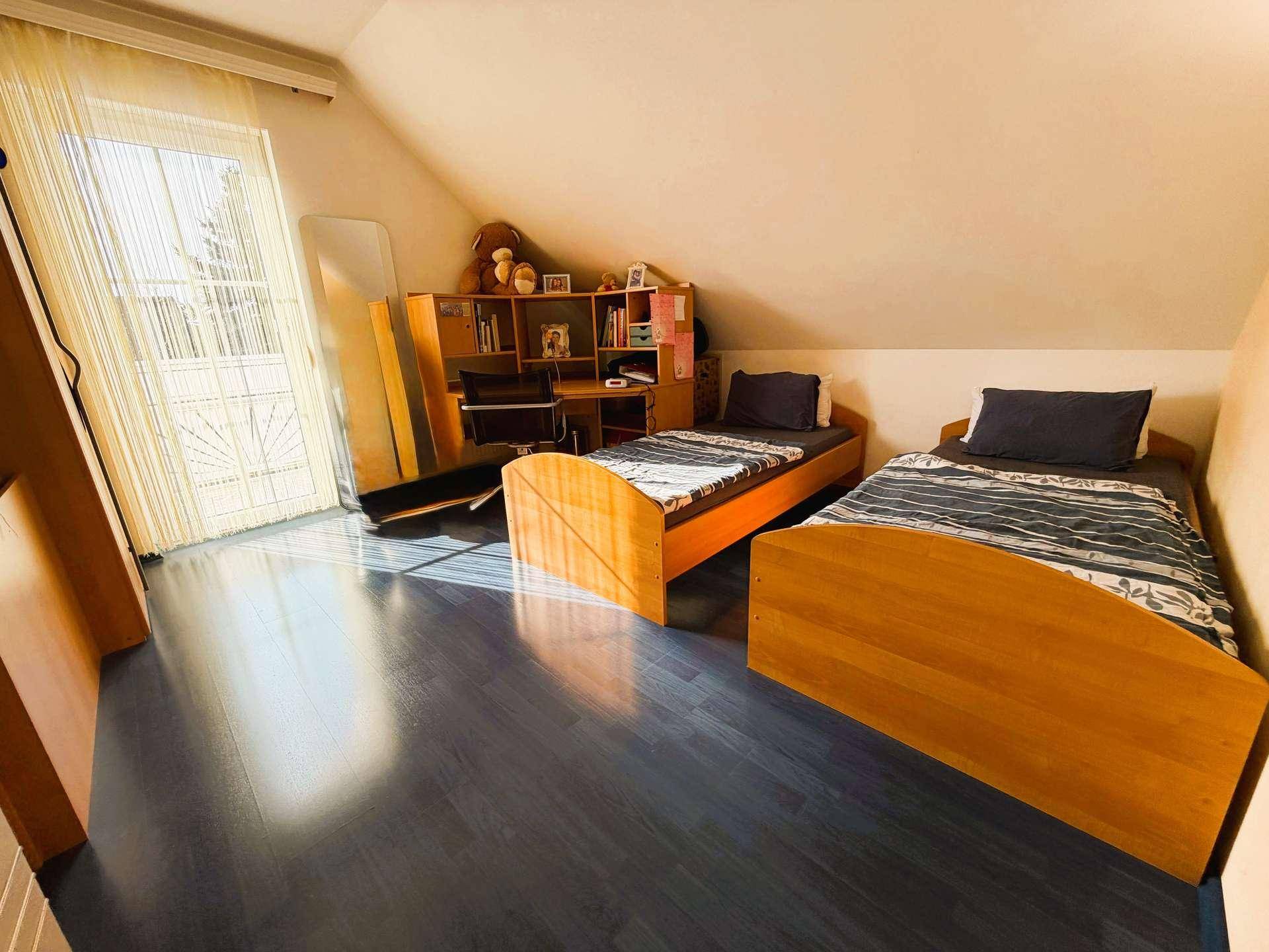 Kinderzimmer im Dachgeschoss mit zwei Einzelbetten, einem Spiegel und Zugang zu einem französischen Balkon.