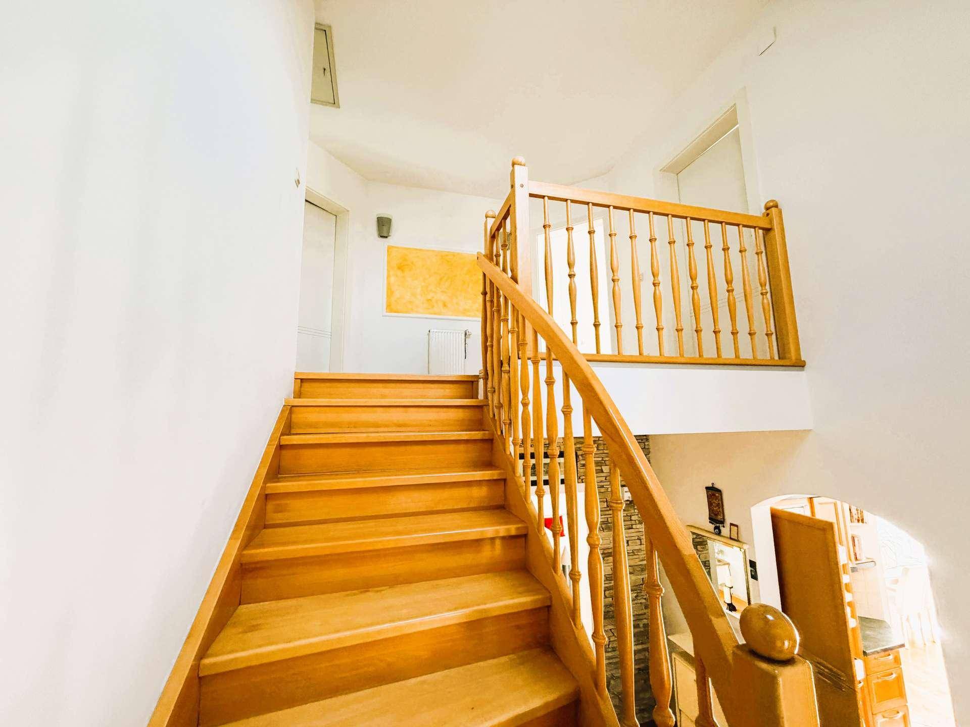 Helle Holztreppe mit klassischem Geländer, die die verschiedenen Ebenen des Hauses verbindet.