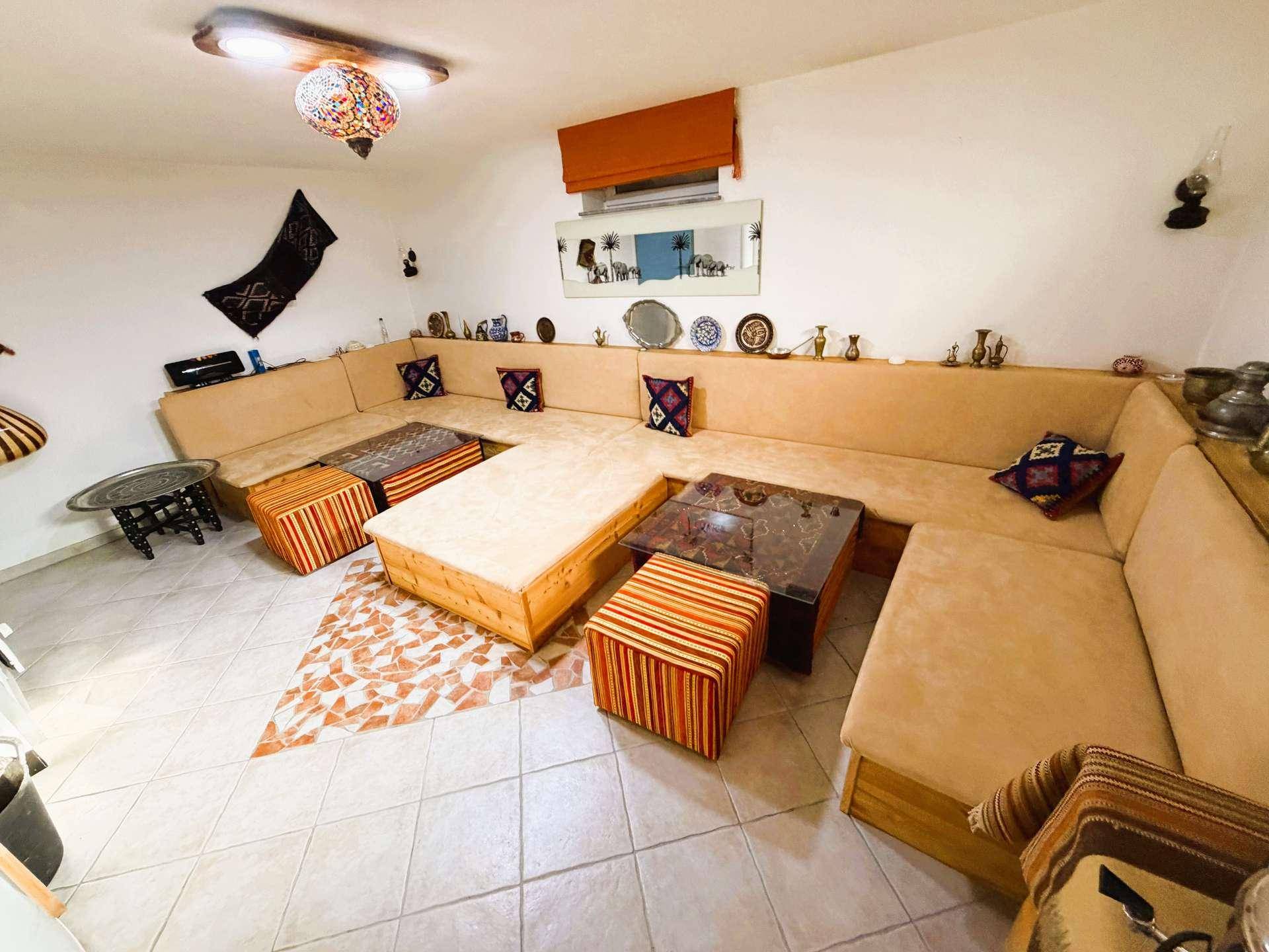 Orientalisch inspiriertes Wohnzimmer mit großer U-förmiger Sitzgruppe, niedrigen Tischen und dekorativer Beleuchtung.