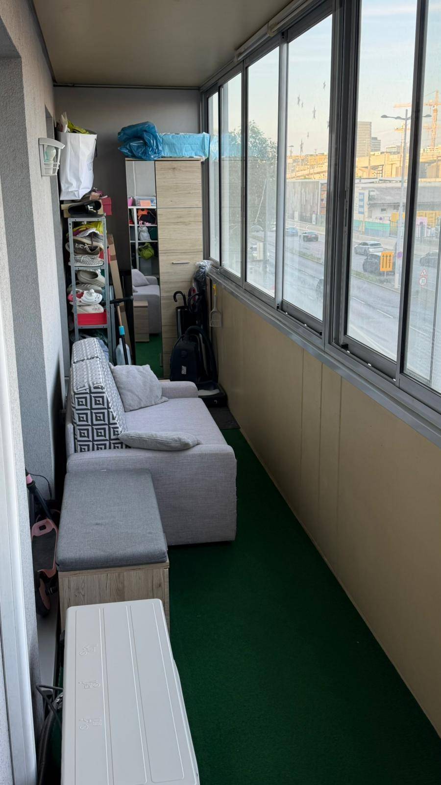 Verglaster Balkon mit Sofa und Stauraum, bietet einen Blick auf die städtische Umgebung.