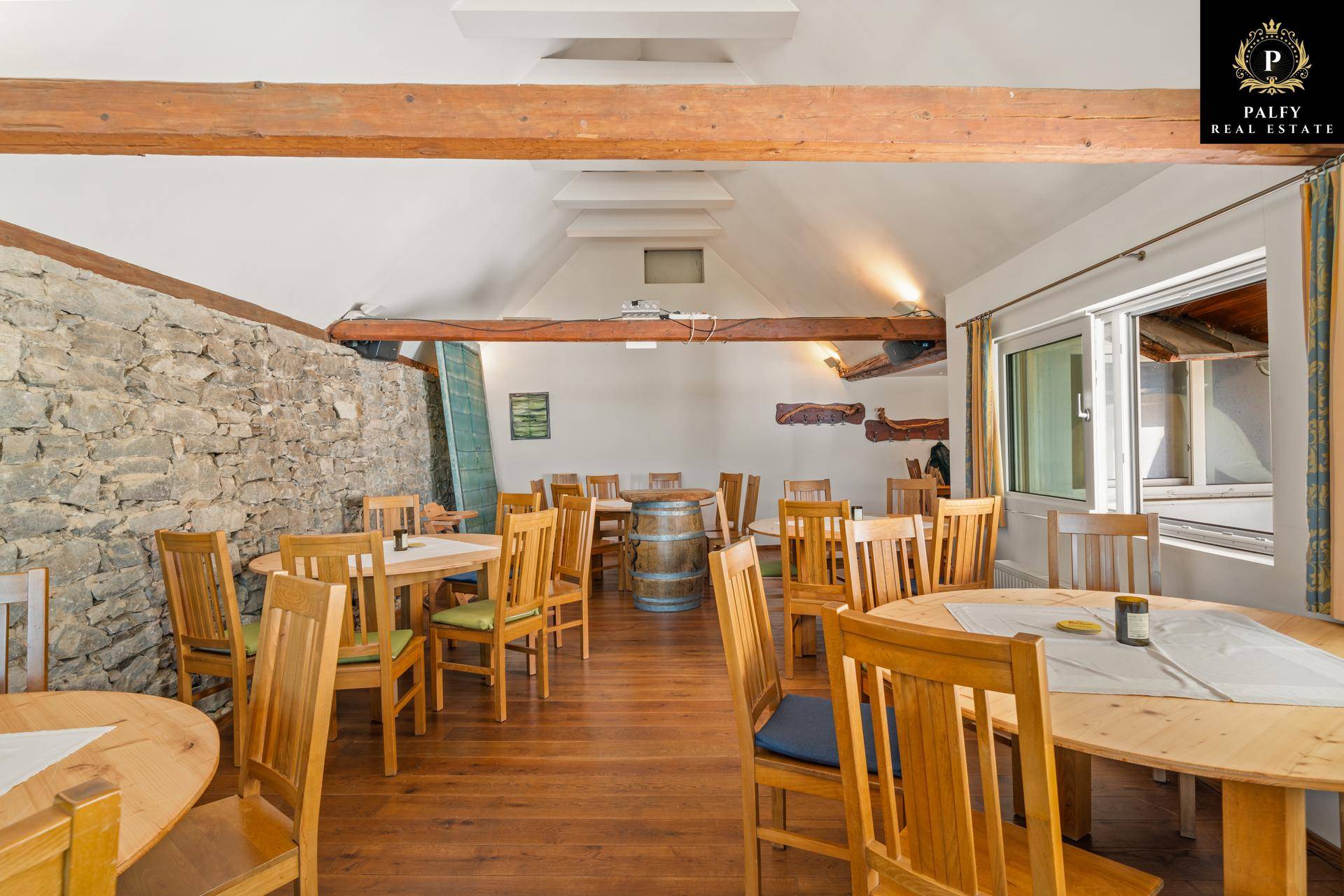 Großer Speisesaal mit Holztischen und Stühlen, Steinwand und Holzbalken an der Decke.