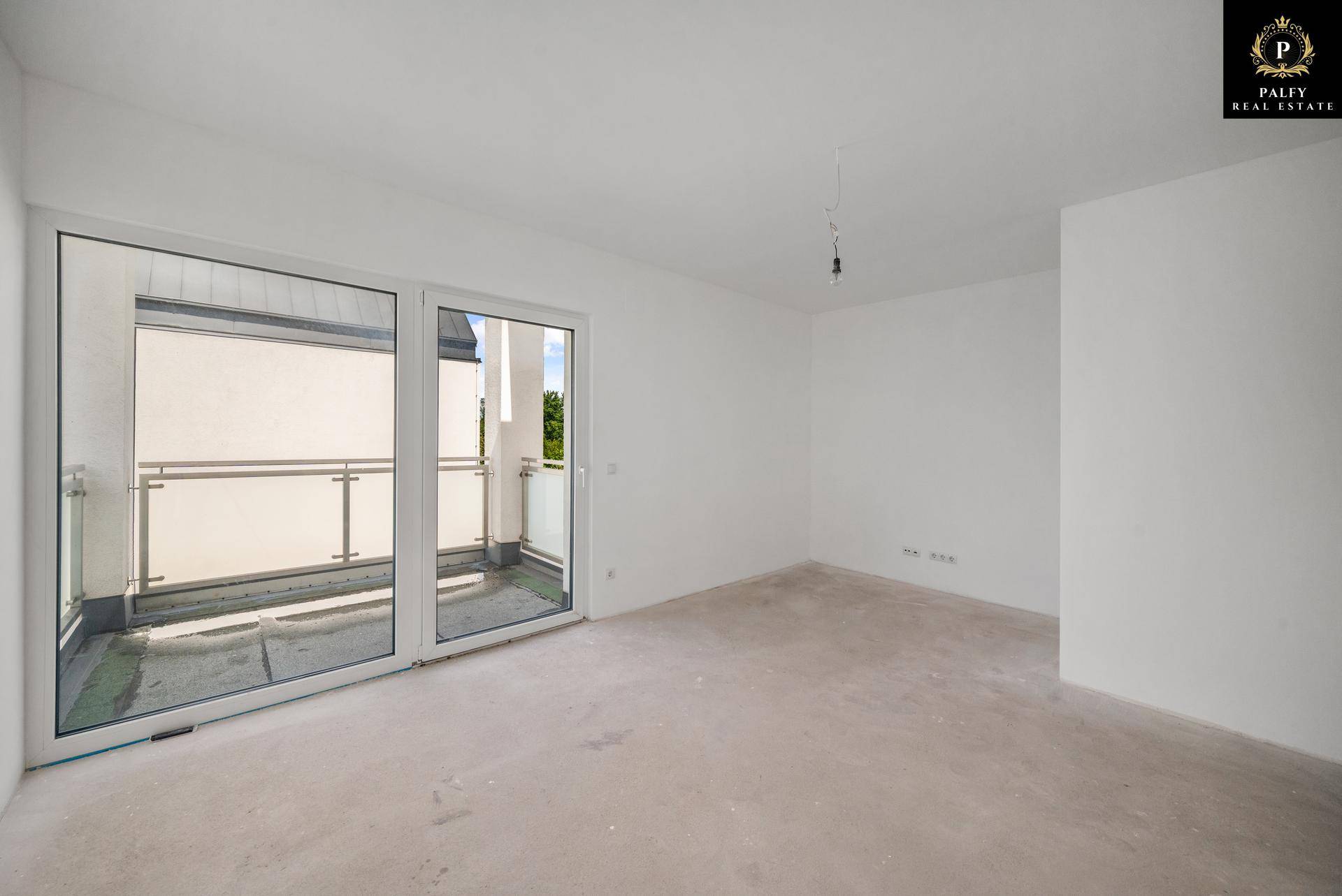 Geräumiger, unmöblierter Raum im Rohbau mit großen Fenstern und Zugang zu einem Balkon.